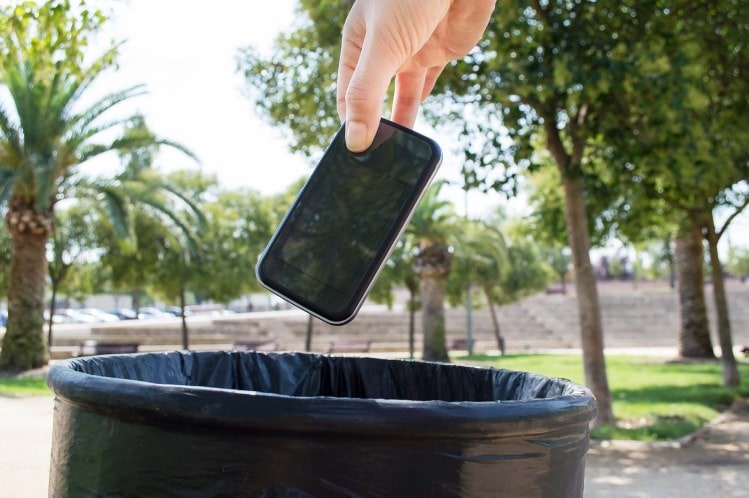 a hand throwing a cellphone into an outside rubbish bin