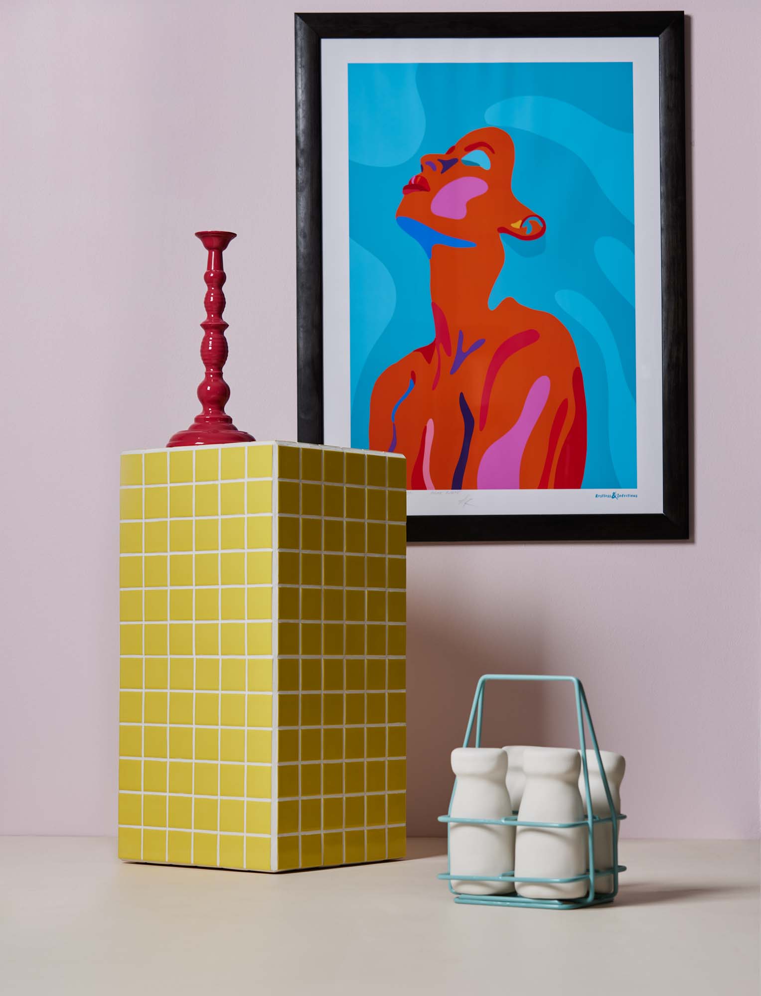 Image with a pale pink wall, a yellow tiled plinth, a candle holder sitting on the plinth, and a milk crate and bottles sculture sitting next to it, a blue and pink painting is on the wall