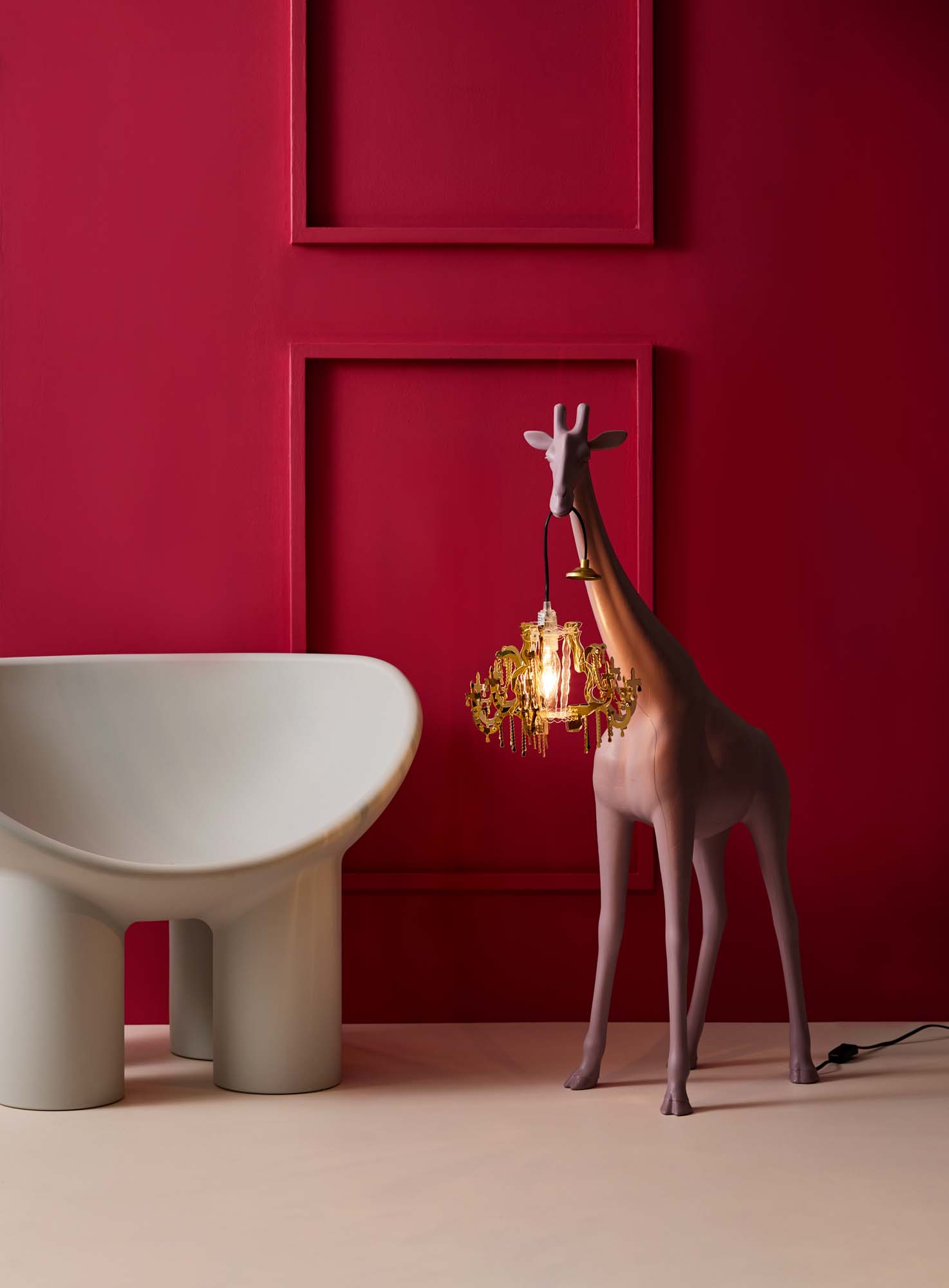 Image with a raspberry red wall, white chair and a giraffe statue