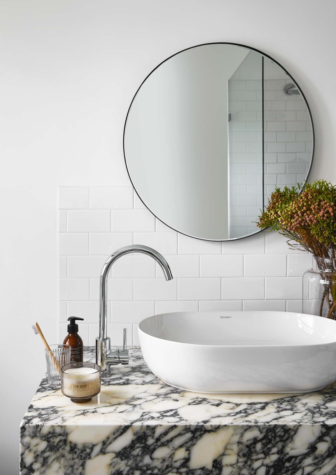 A white and black veined bathroom bench with a white sink and a round mirror on the wall
