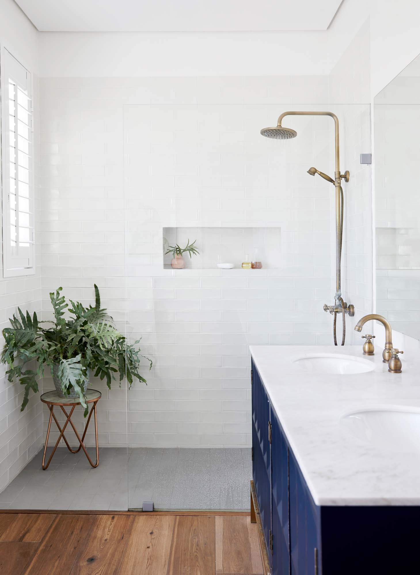 A large walk-in shower that is tiled with white, textured tiles, a deep navy vanity is on the right with white stone benchtop