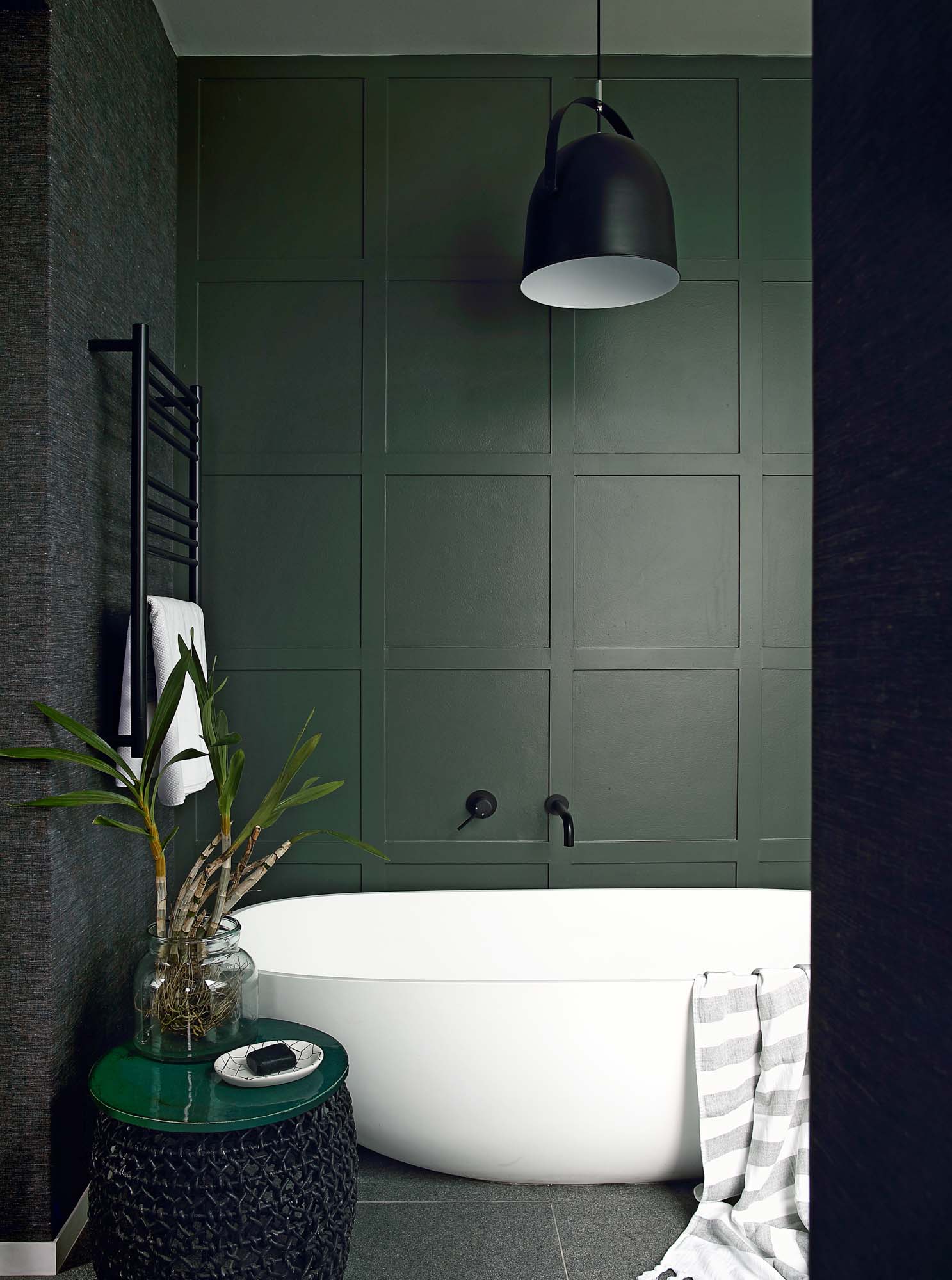 A green bathroom with forest green painted walls and dark tiles and a white freestanding bath