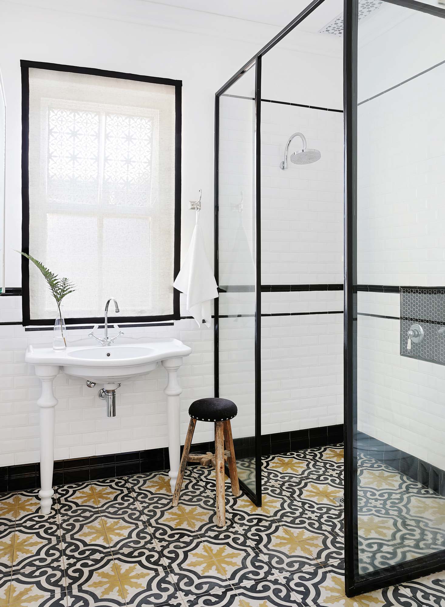 A bathroom with a black and glass shower screen, a white freestanding vanity sink, and navy and yellow patterned tiles
