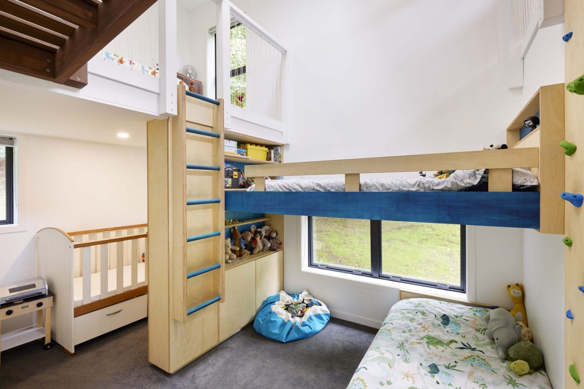 A children's room with a cot, multiple beds and a rock climbing wall