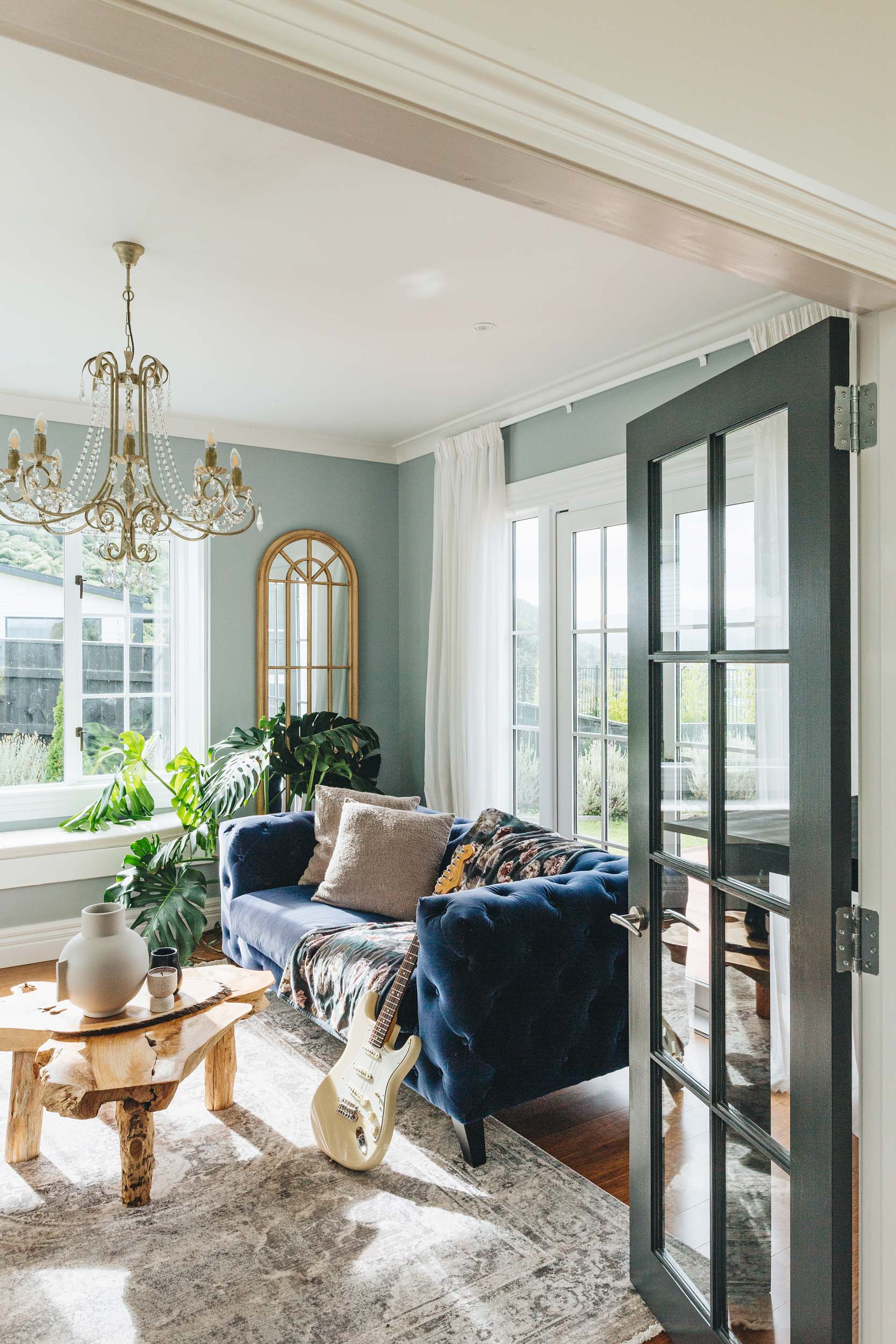 Sitting room with blue velvet couch, with a guitar leaning against it. There is a wooden coffee table and blue turkish rug on the floor