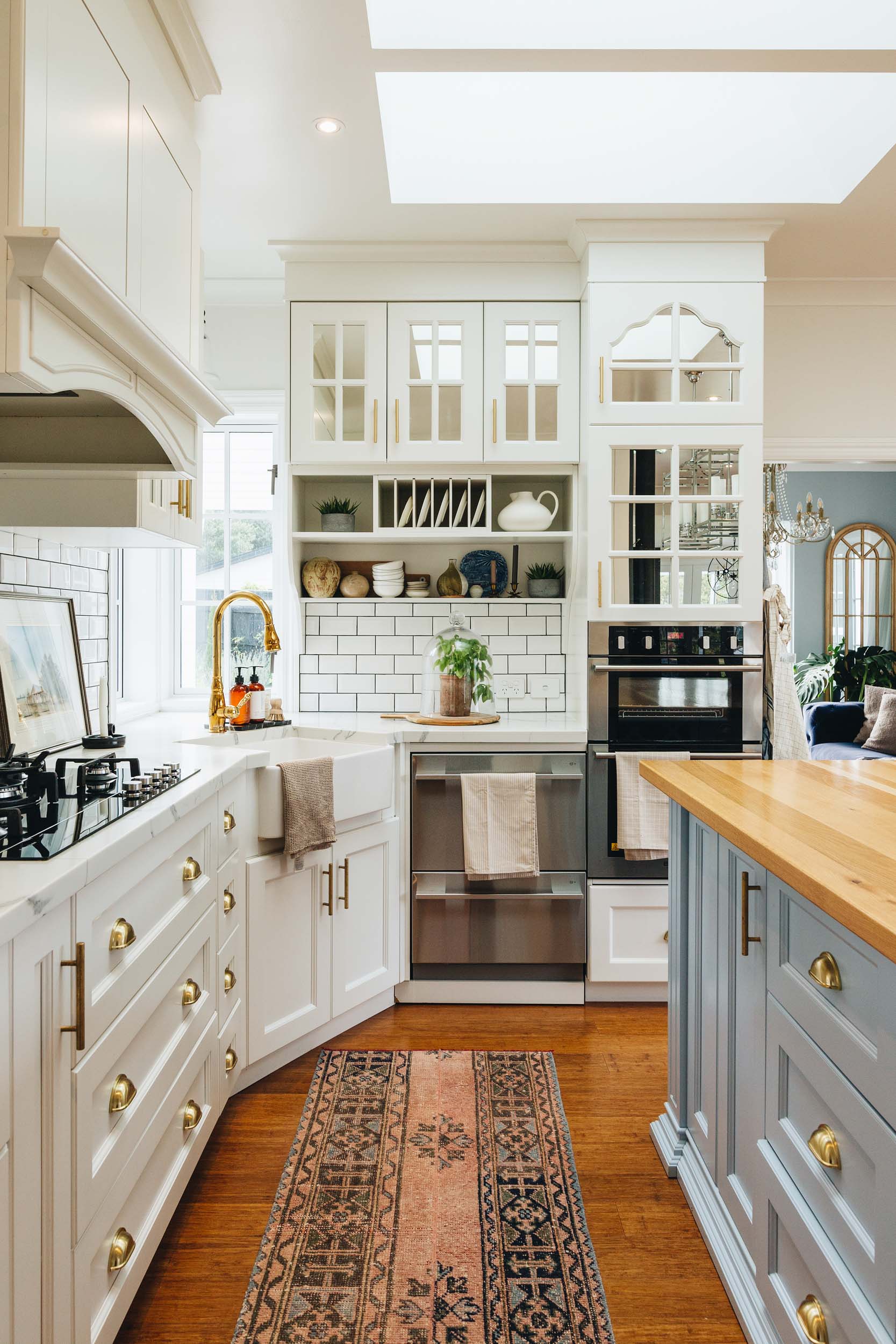 white kitchen cabinets with brass hardware. White subway tiles, a sink is in the corner