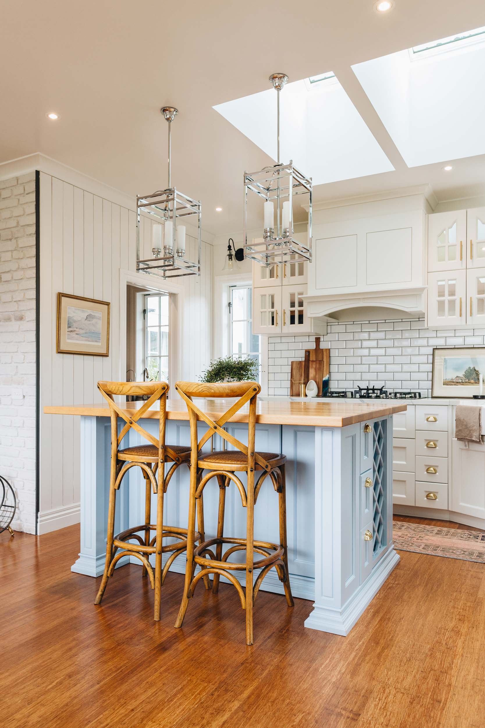 Baby blue kitchen island with the rest of the cabinets a white shade with brass hardware, white subway tiles