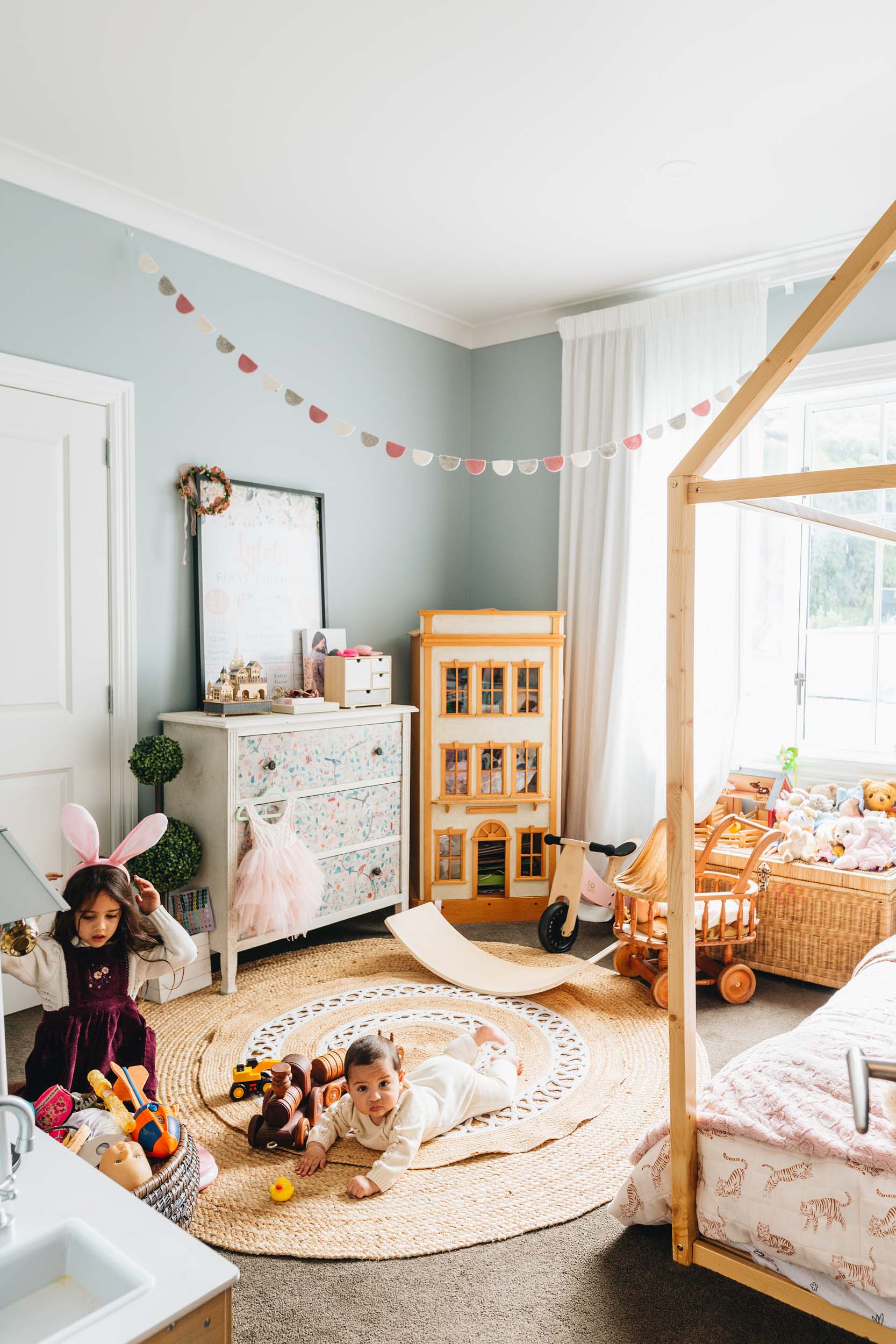 Little girls room with a circular rattan rug in the centre, house bed frame, doll house in the corner next to a dresser