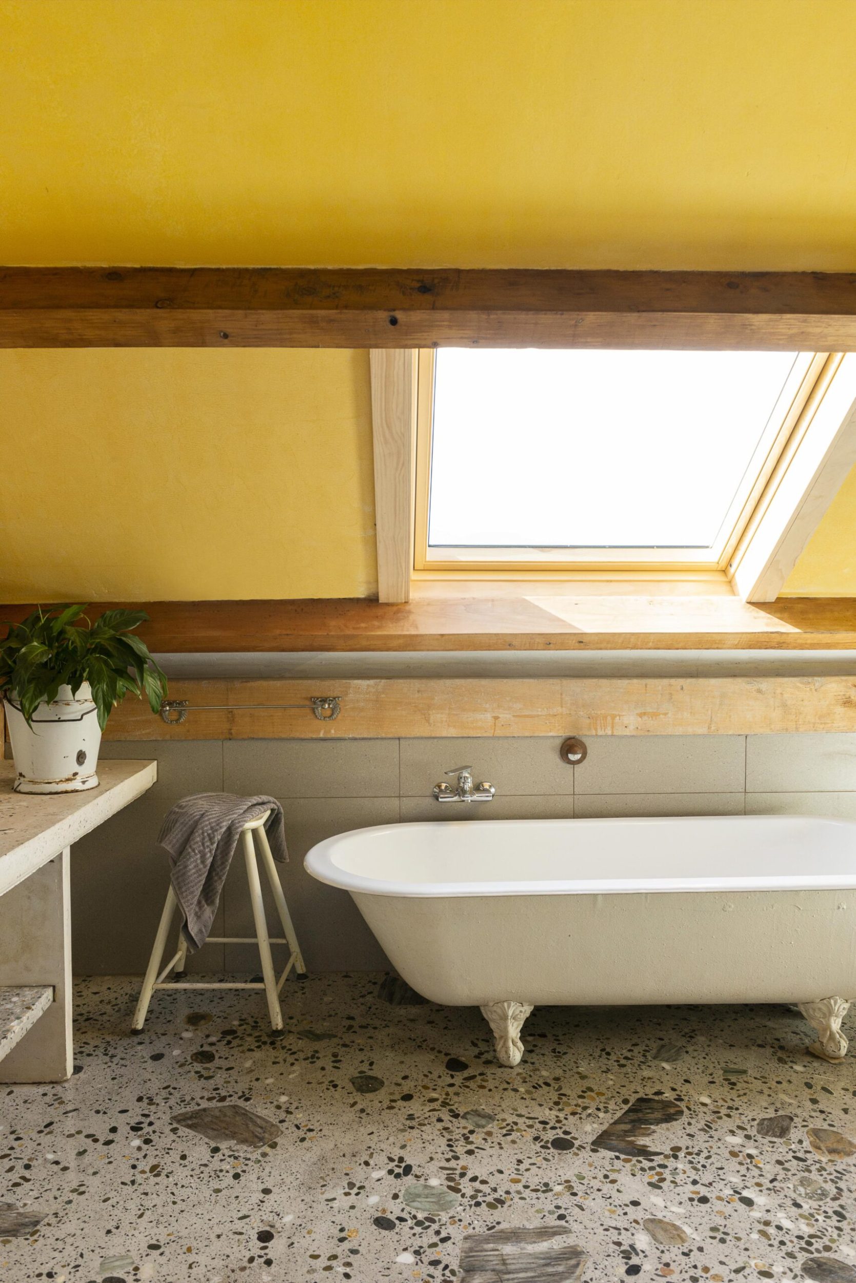 A bathroom with yellow walls, grey floors, a claw foot tub, angled ceiling and a ceiling night