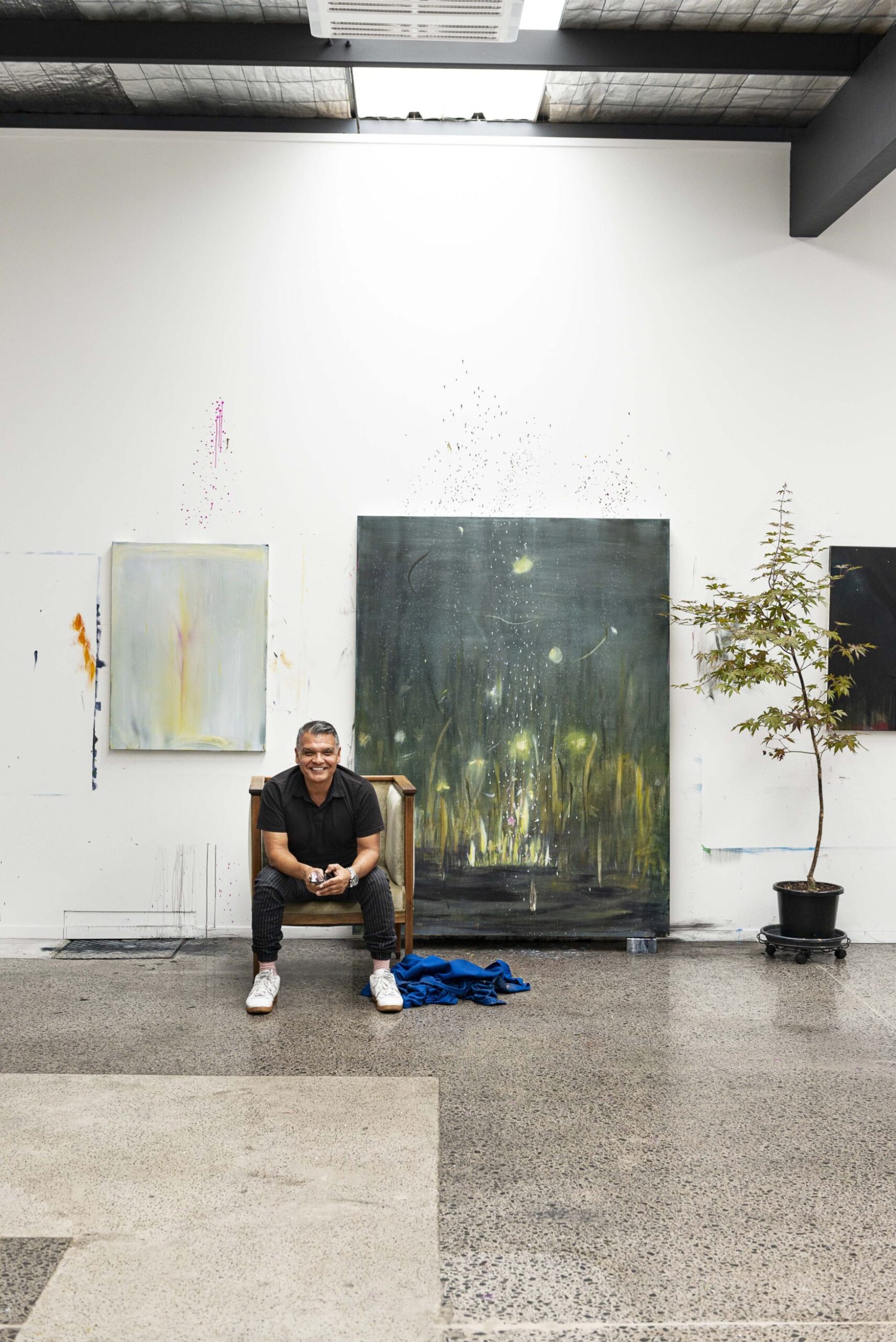 Cruz Jimenez sitting on a chair in front of his artwork