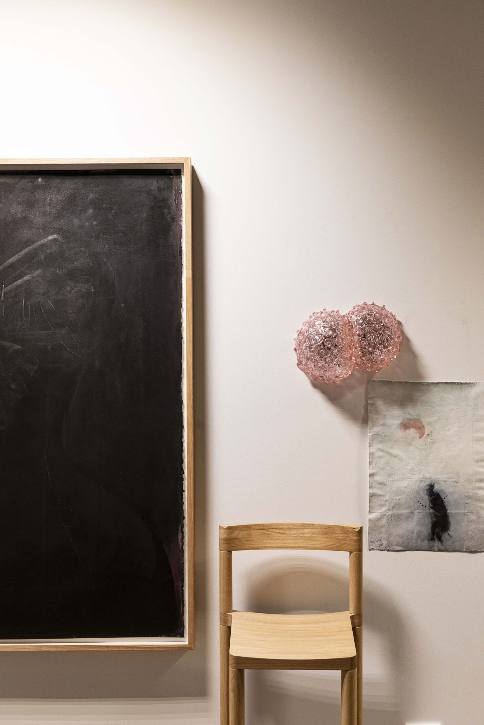 Black painting hangs next to wooden chair and pink bubble artwork