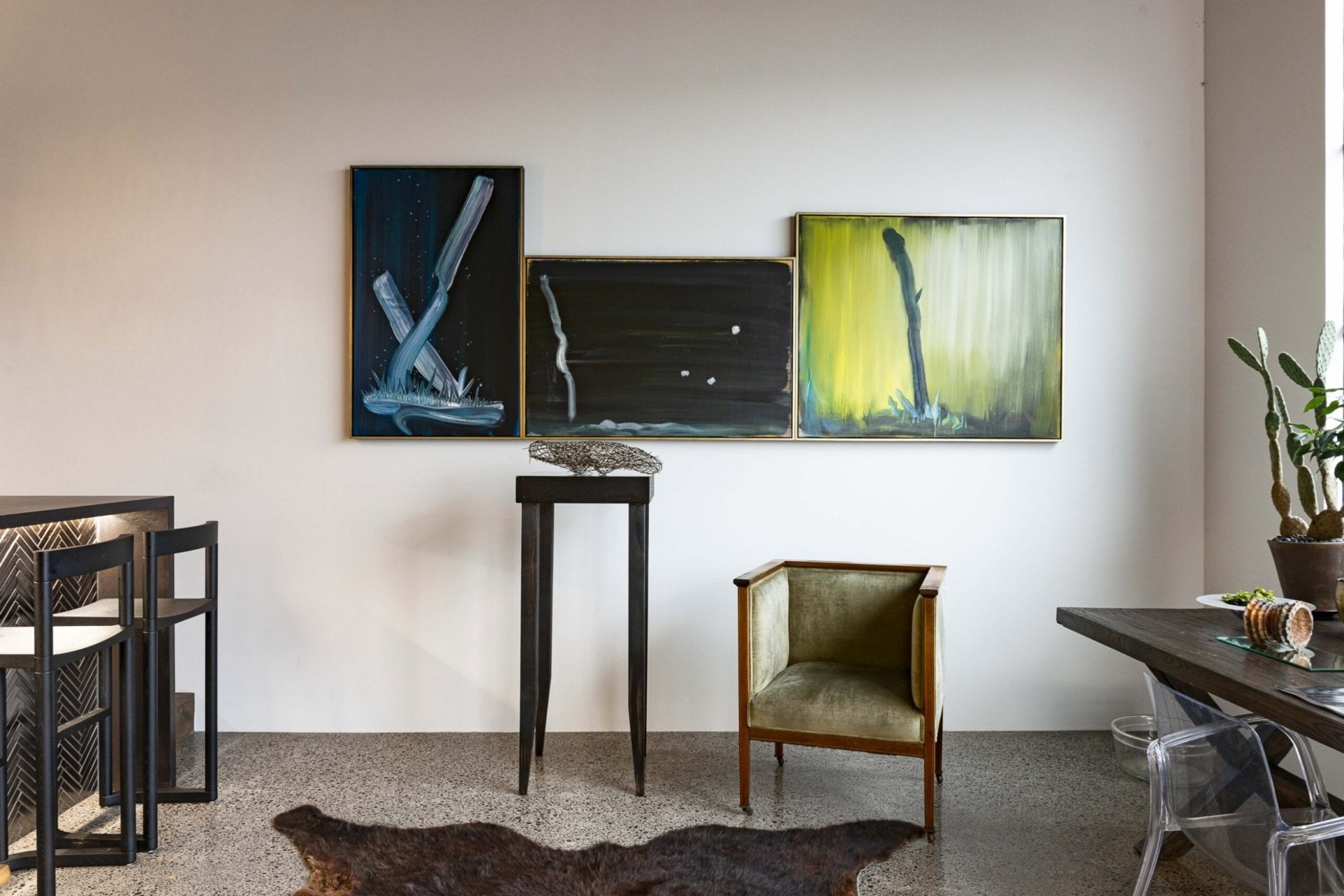 Three paintings hanging on the wall with green velvet chair below