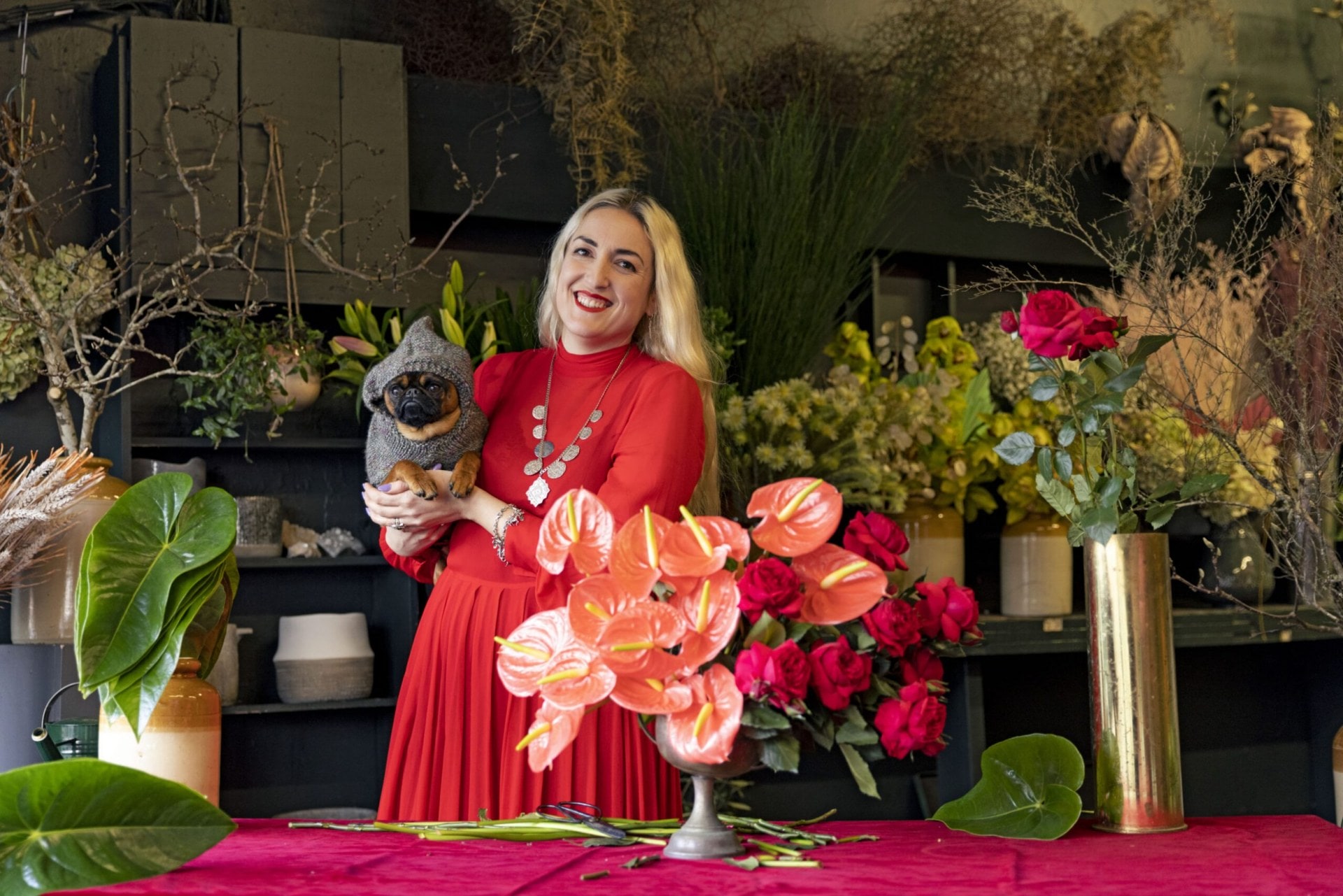 Georgie Malyon holding her dog Roky standing in front of a red table with a floral arrangement