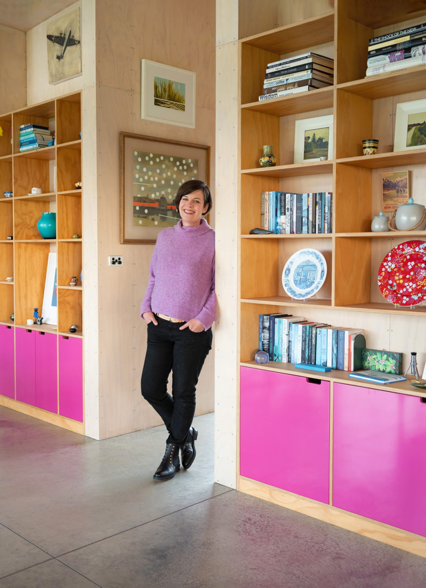 Catherine Robertson standing by inbuilt wood and pink shelving in her home