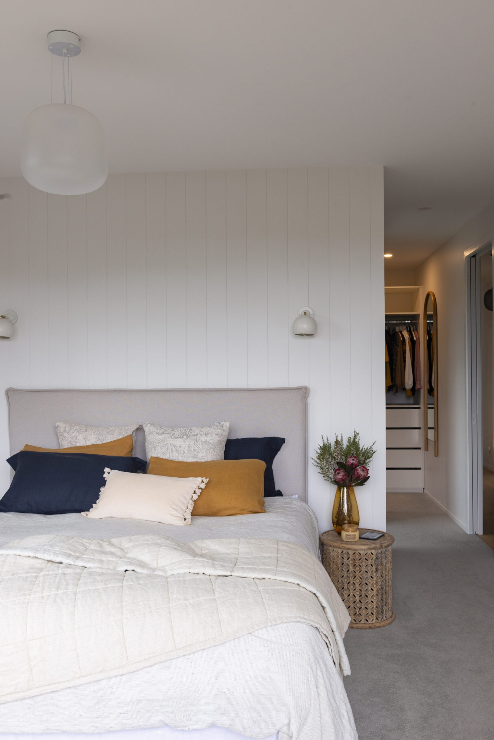 Bedroom with grey carpet, white wall panels, a bed with white bedsheets and colourful accent pillows