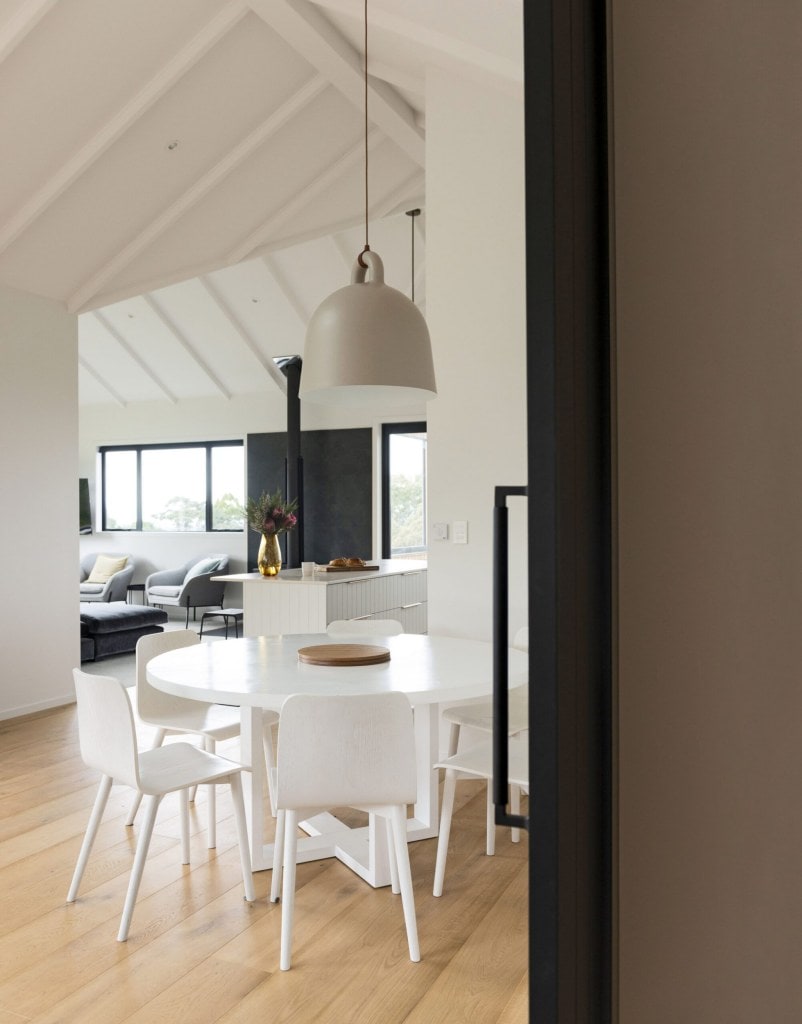 An open plan dining room with white walls, vaulted ceilings and a round white dining table