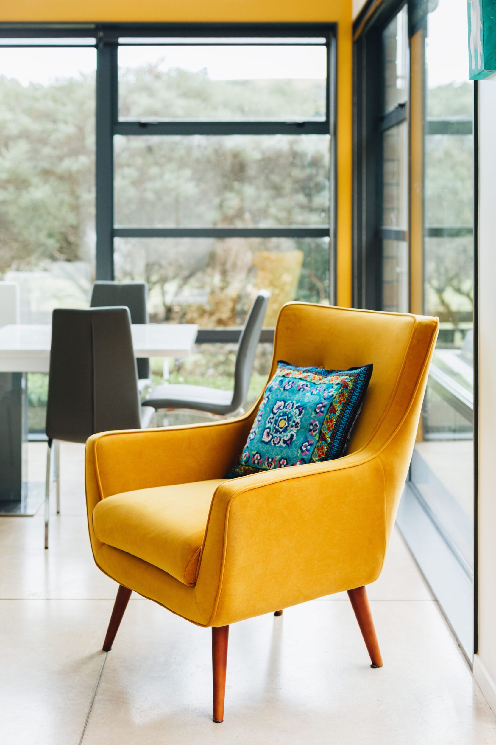 A yellow chair with brown wood legs and a blue cushion