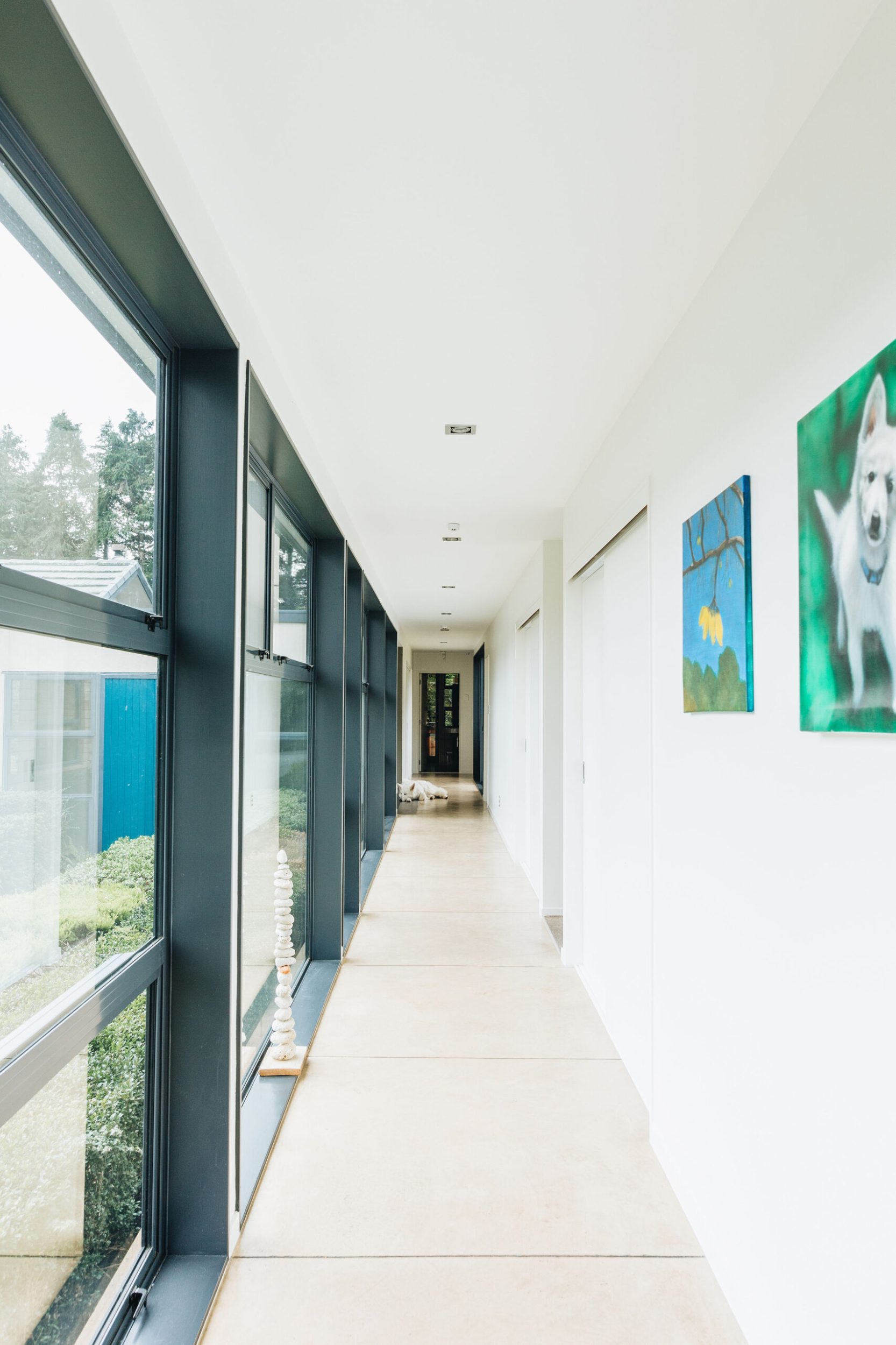 A long hallway with white walls, large grey floor tiles and large windows 