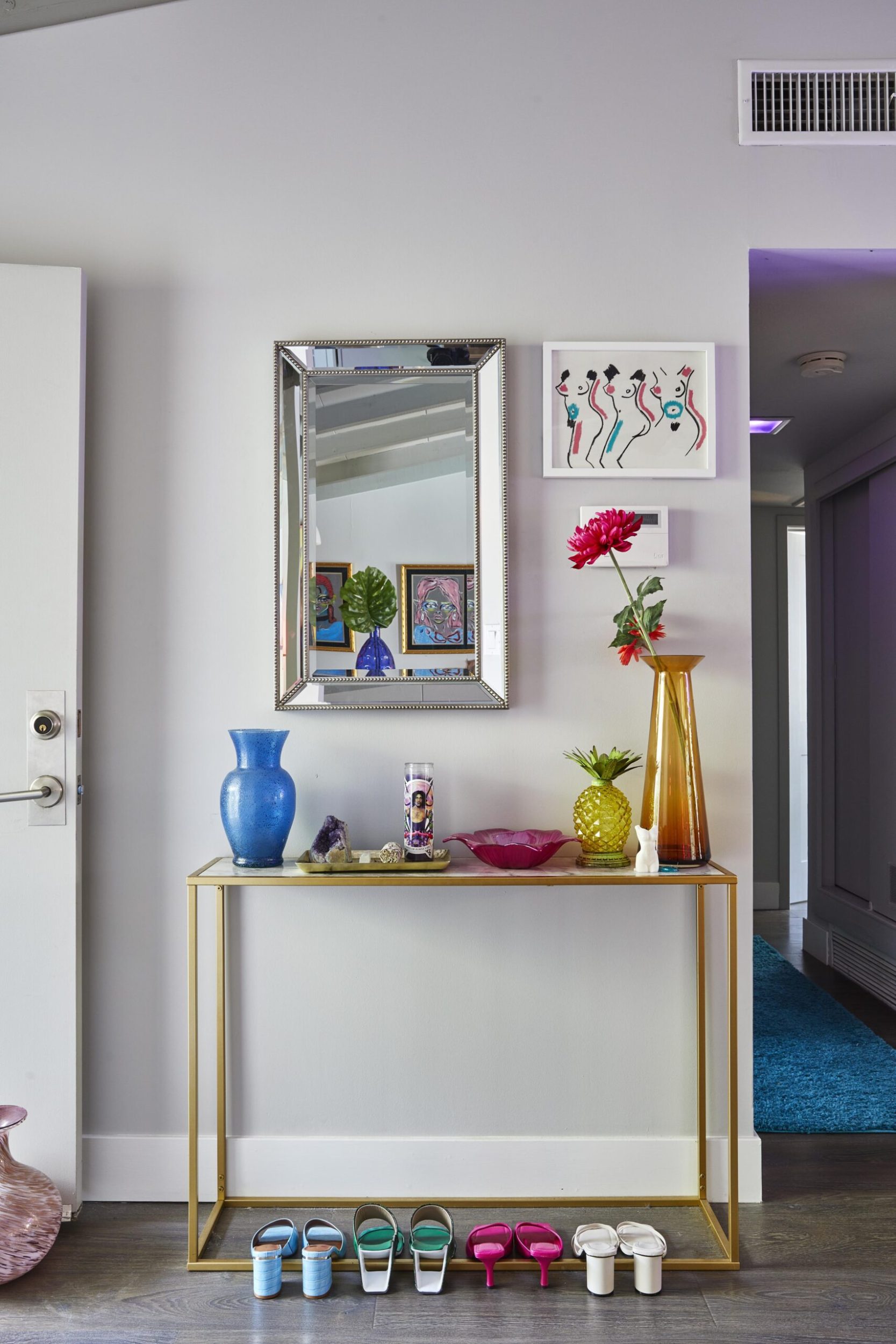 Parris Goebel home entryway with a gold side table, hanging mirror and colourful shoes and decor