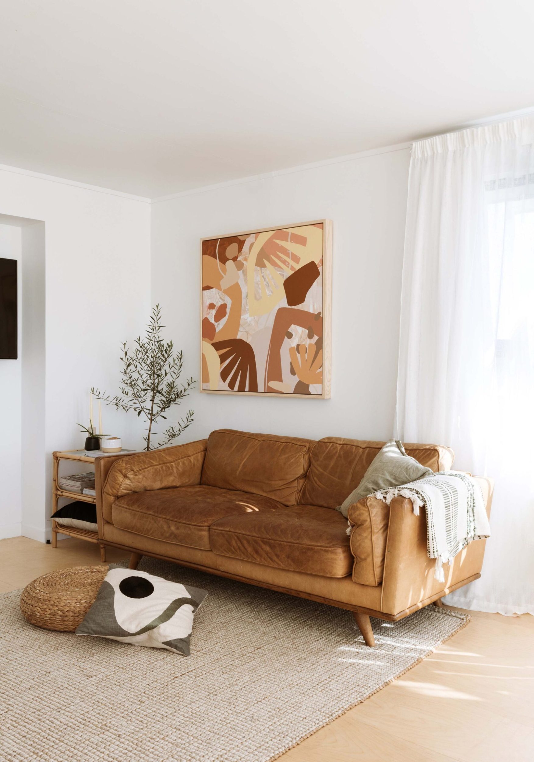 Living room with a large tan leather couch, a large piece of art above, and ply flooring with a natural rug