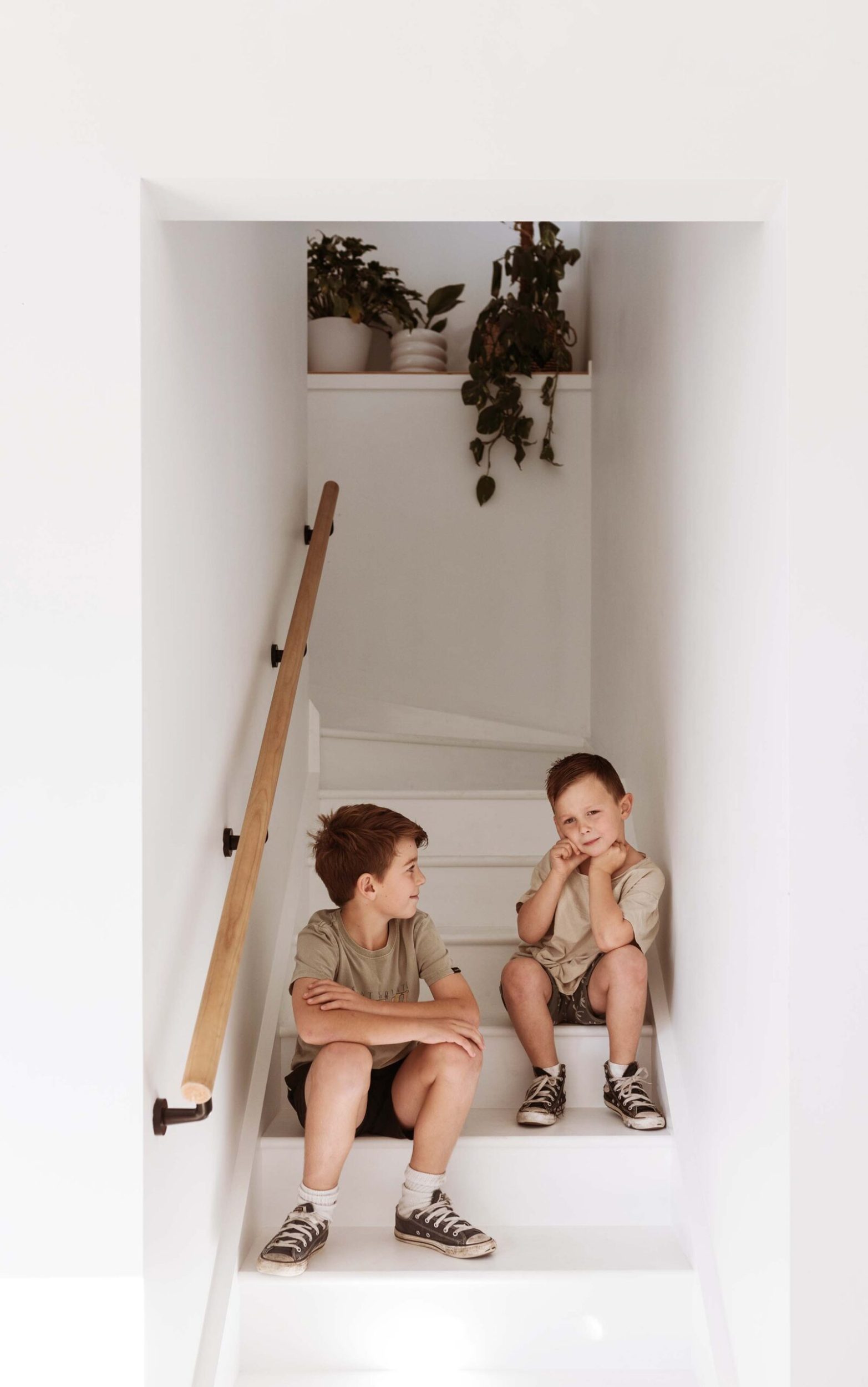 two kids sitting on painted white stairs in a white painted stairwell