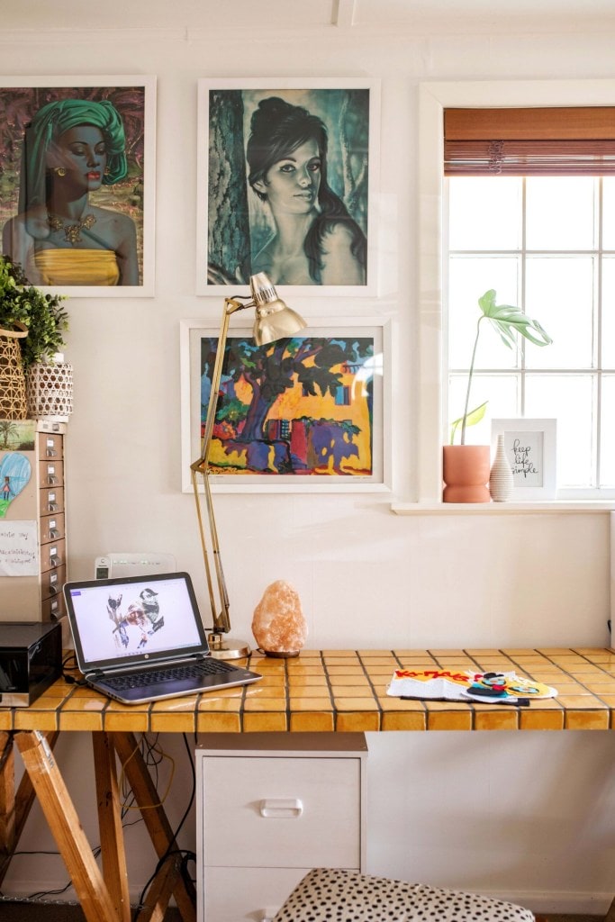 A desk made from two sawhorses and a workbench made of a slab of mustard tiles the walls of the studio are also adorned with artwork