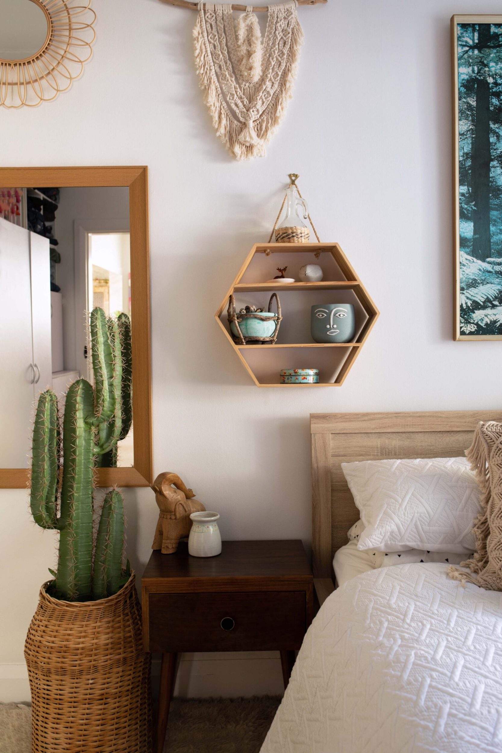 A bedroom with white walls, a hanging wooden hexagonal decor and a large cactus