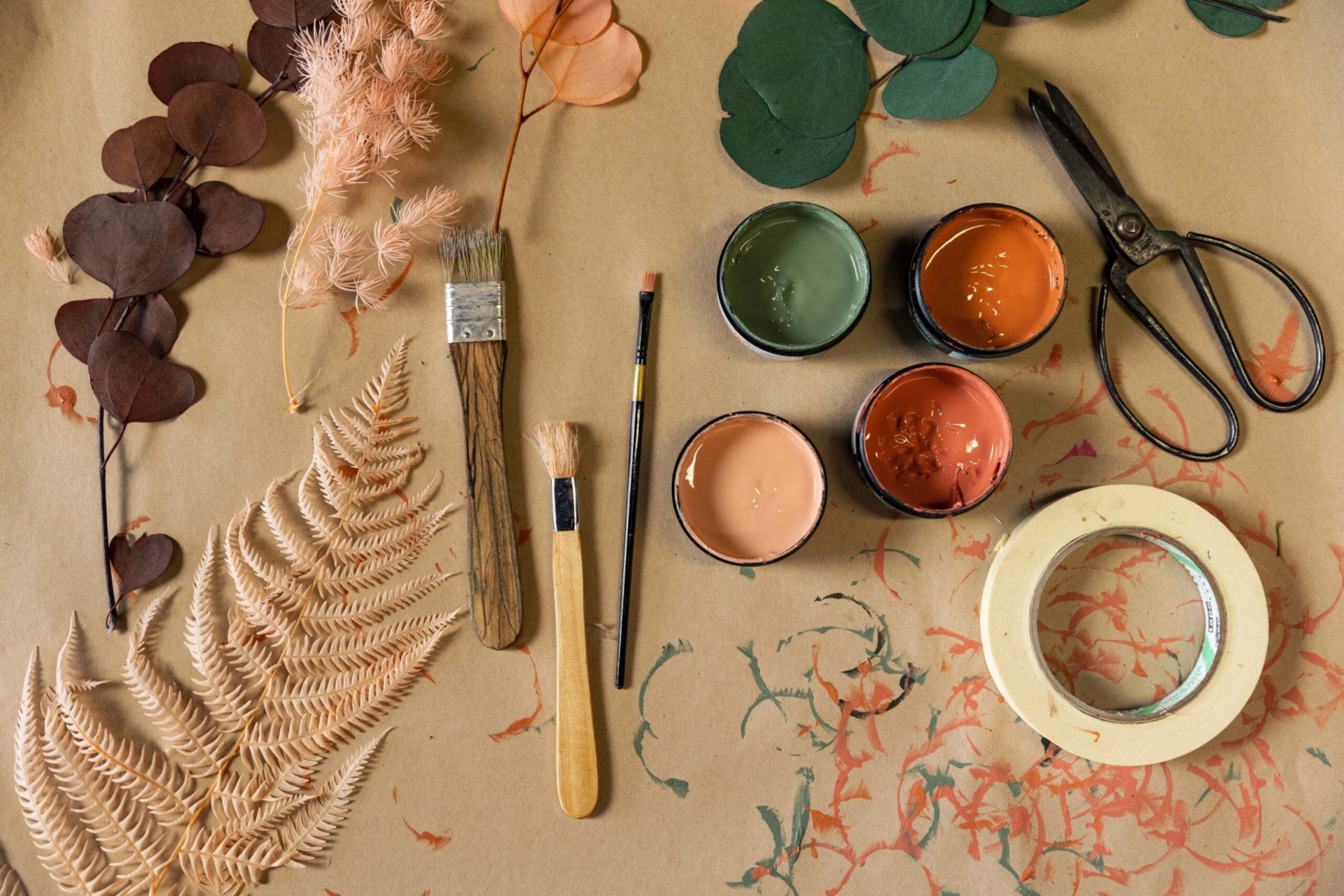 A flat lay of various botanicals, paint, paint brushes, tape and scissors