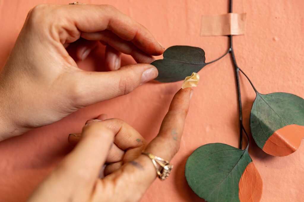 using tape to attach a eucalyptus clipping to the wall