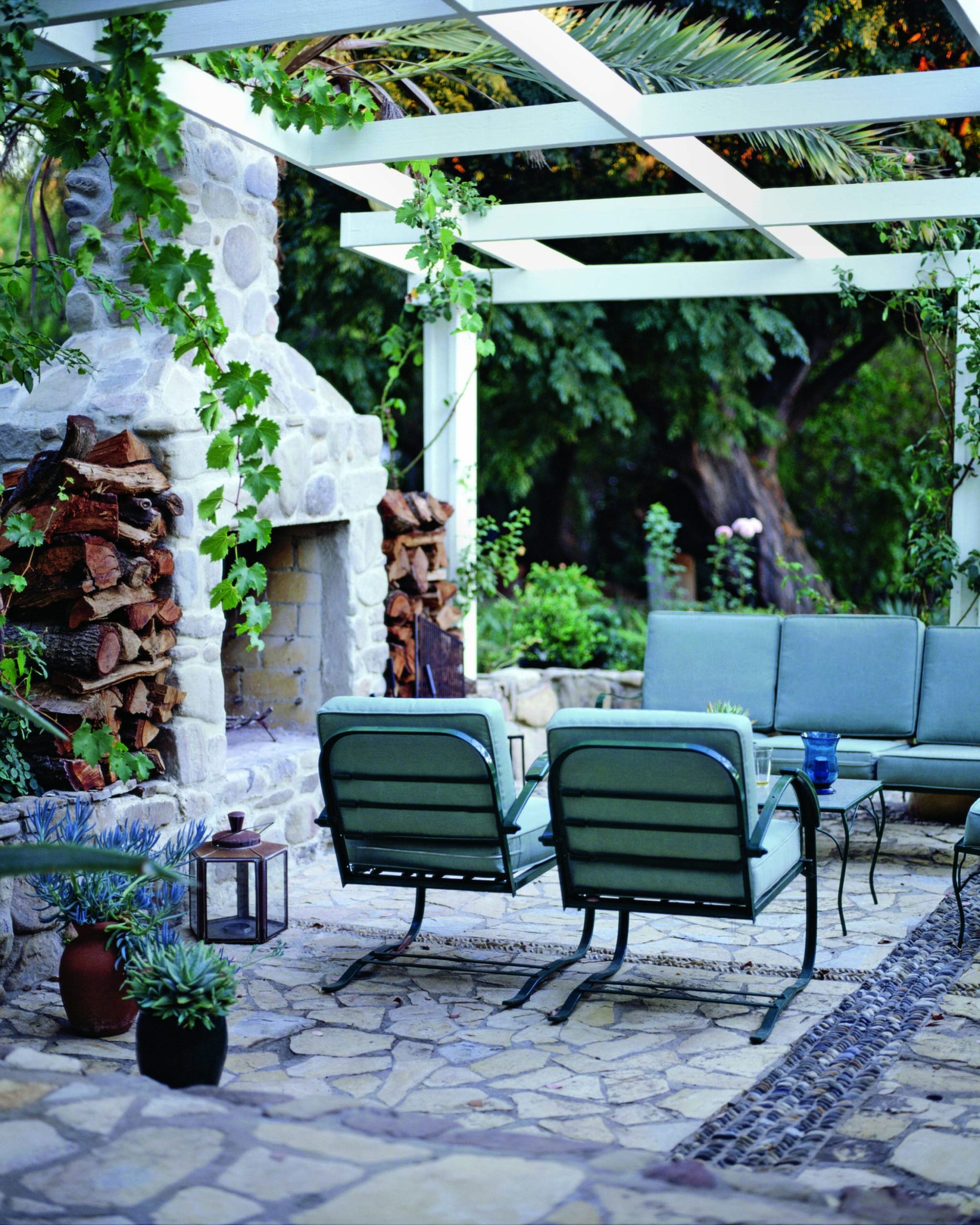 An outdoor stone fireplace with hanging plants and a seating area in front of the fireplace