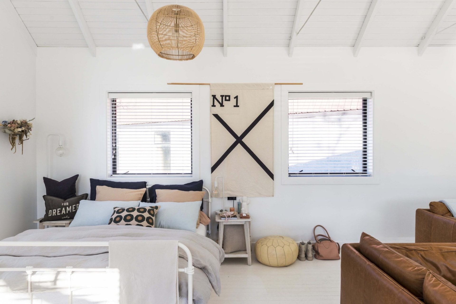 A white metal bed dressed in grey linens, with a large No 1 wall hanging on the wall