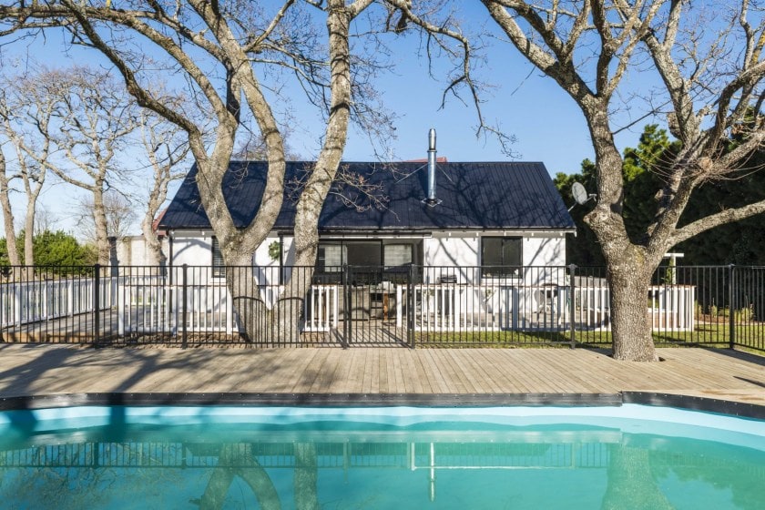 Blue swimming pool with a house in the background with two large trees on either side