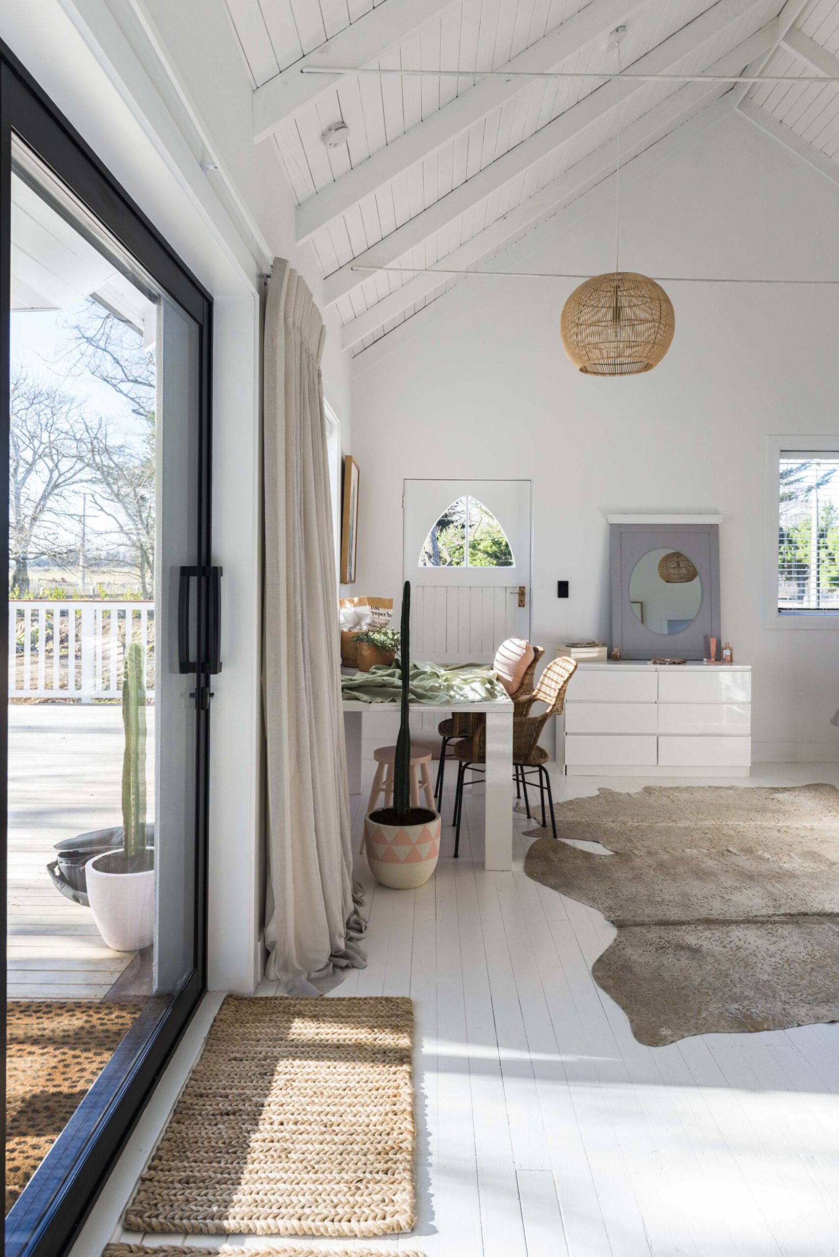 White room with doors to the left, cathedral ceilings, and a desk at the end of the room and a dresser