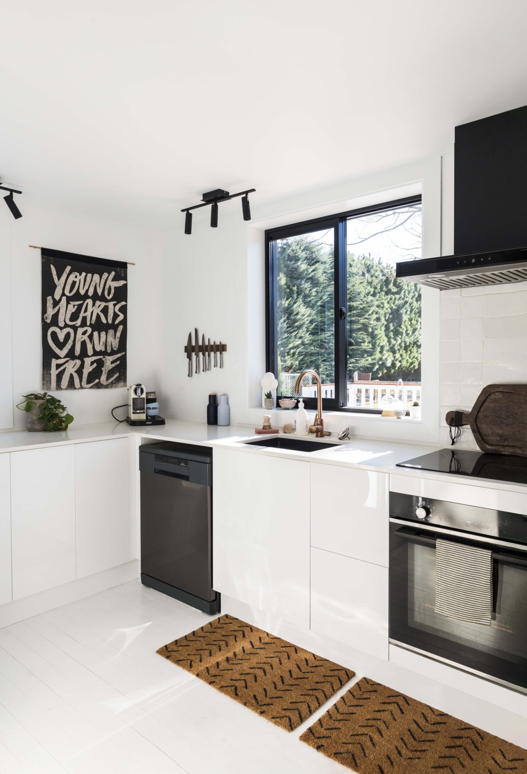 A white kitchen cabinet with black appliances and white painted Rimu floors