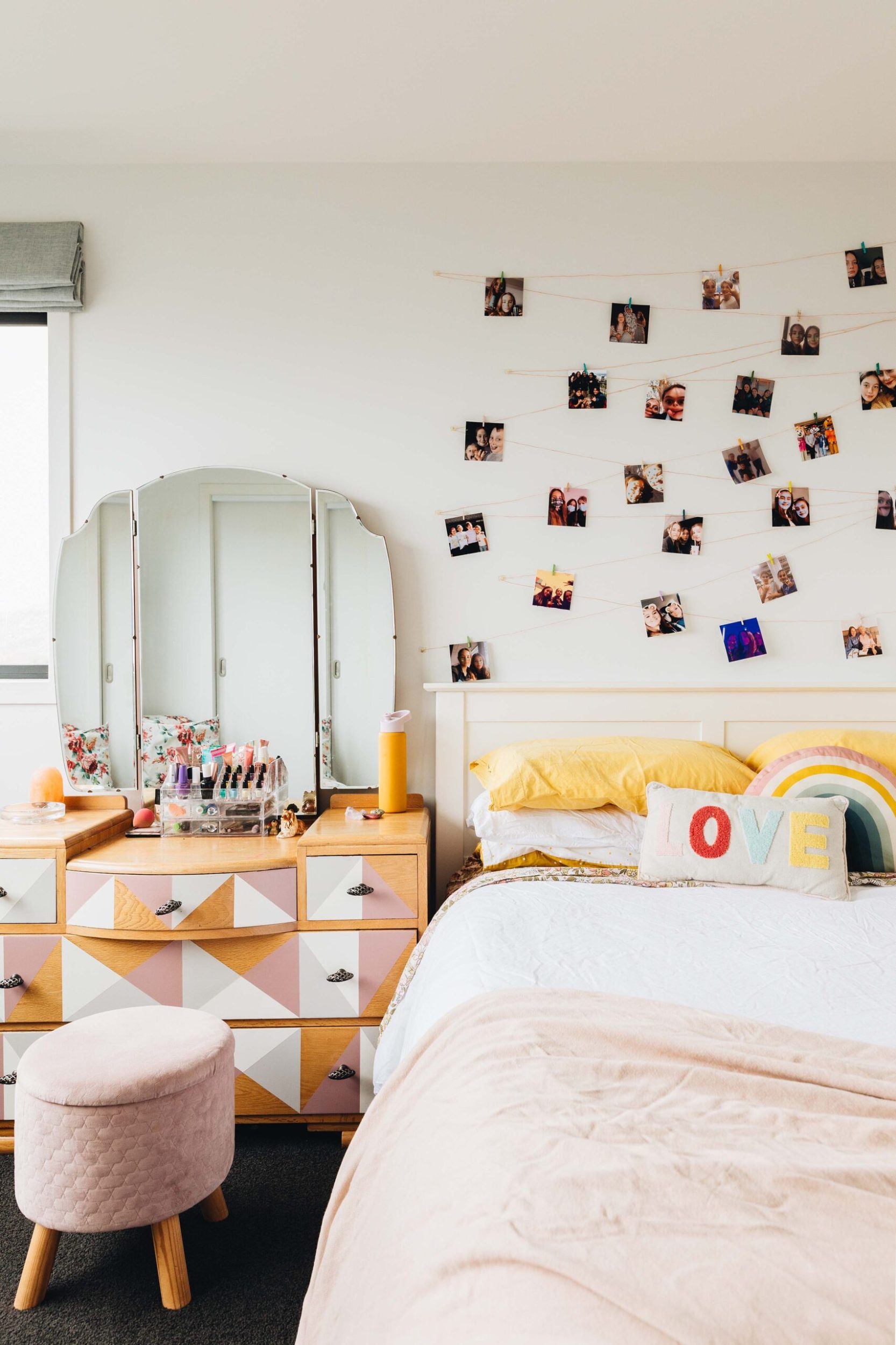 A little girls' room with a large bed and photos hanging on the wall, a pink and orange dresser with a pink stool
