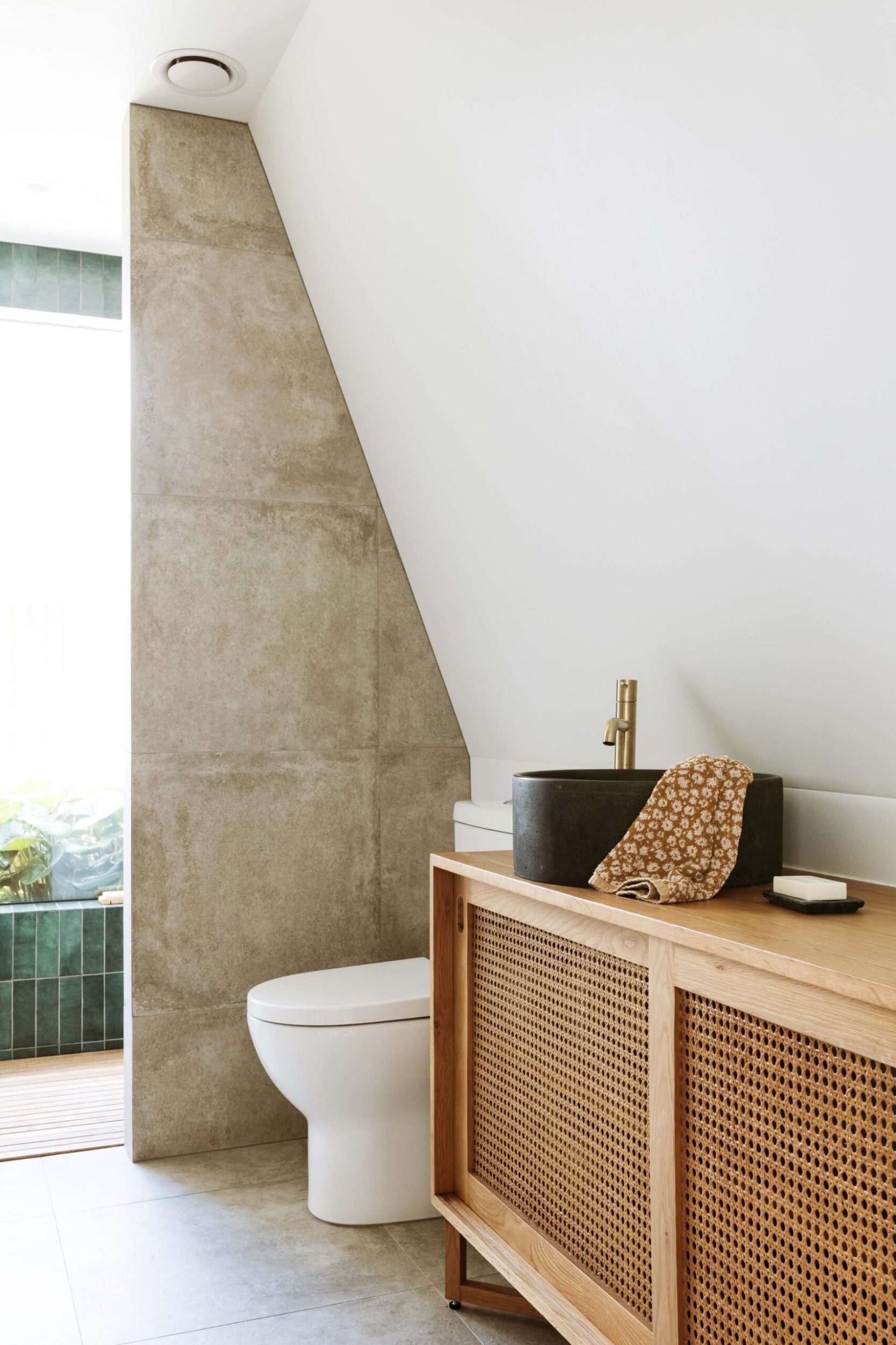A wooden and rattan bathroom vanity with large format grey tiles and a white toilet