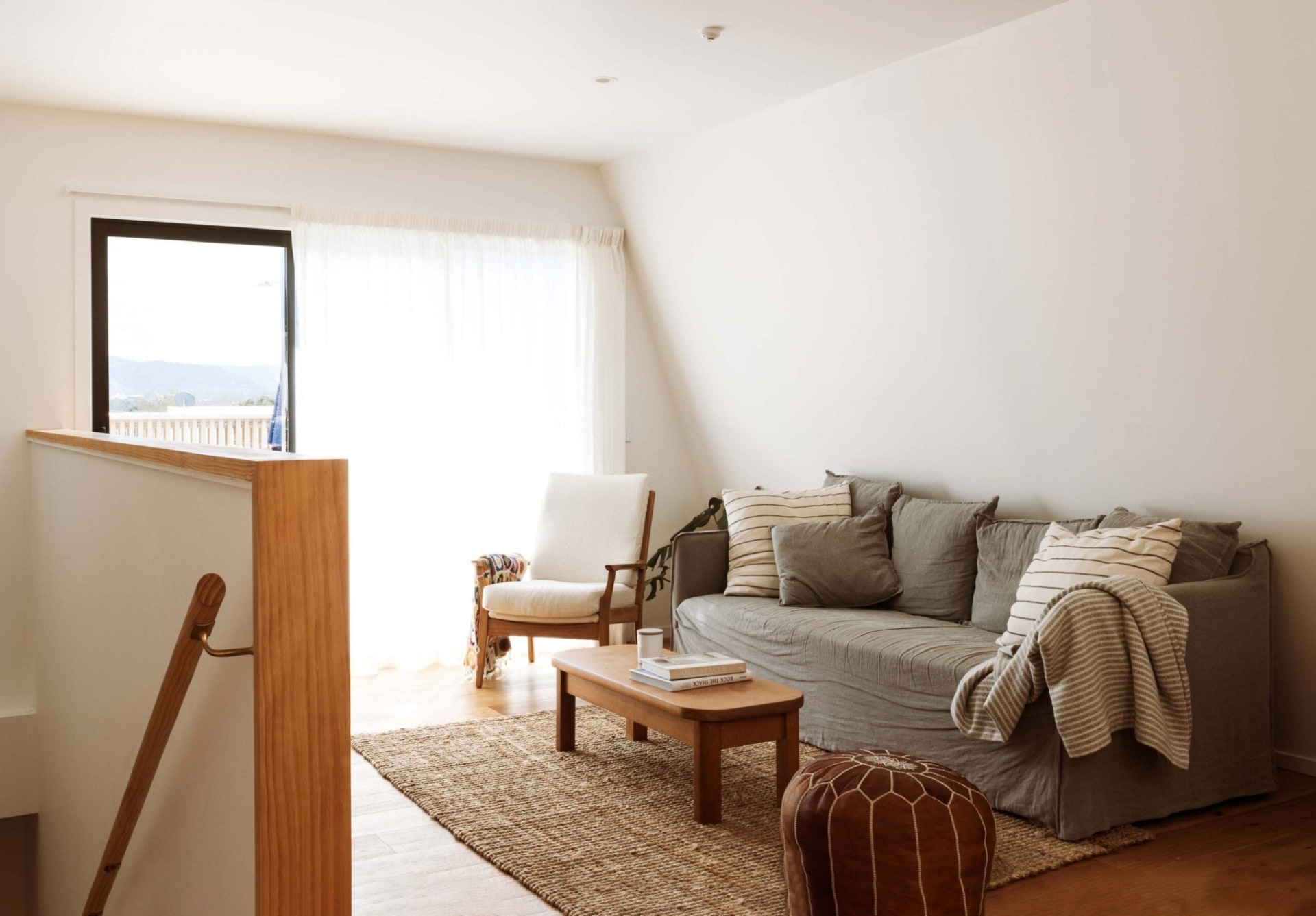 A white living room with a grey couch and wooden coffee table and moroccan poof