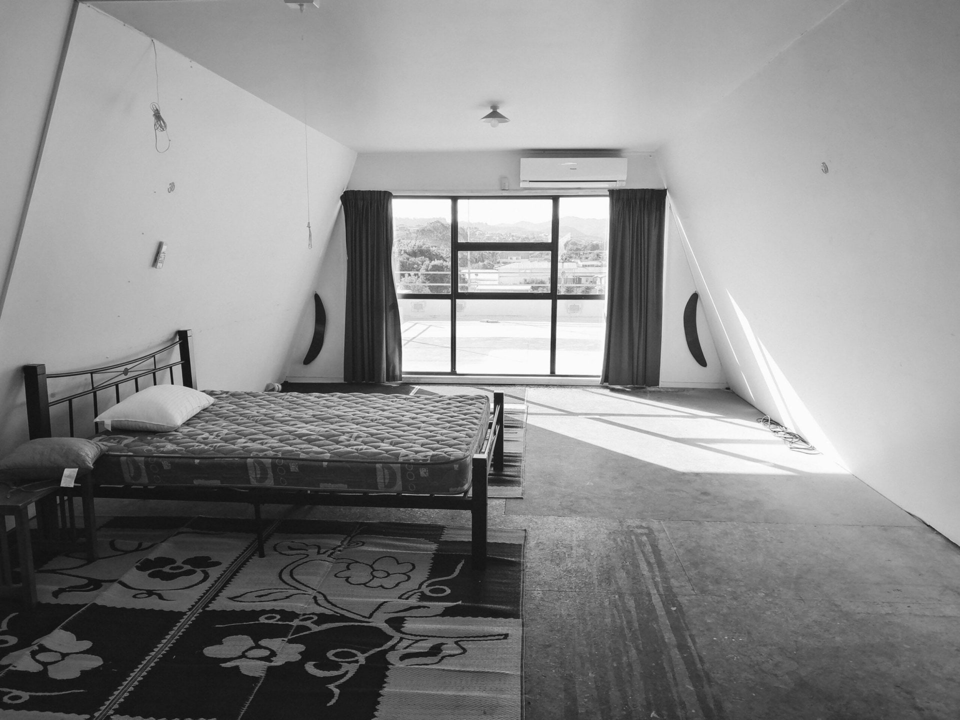 Image in black and white of a long bedroom with metal bed frame to the left