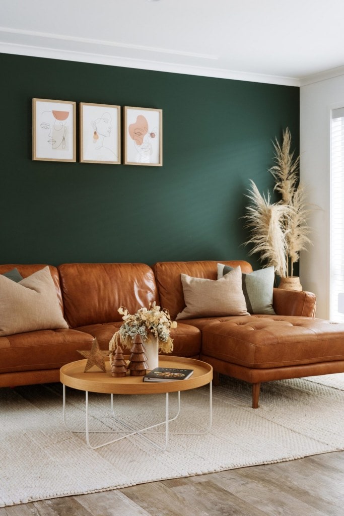 A deep green wall is the backdrop to a tan leather sofa