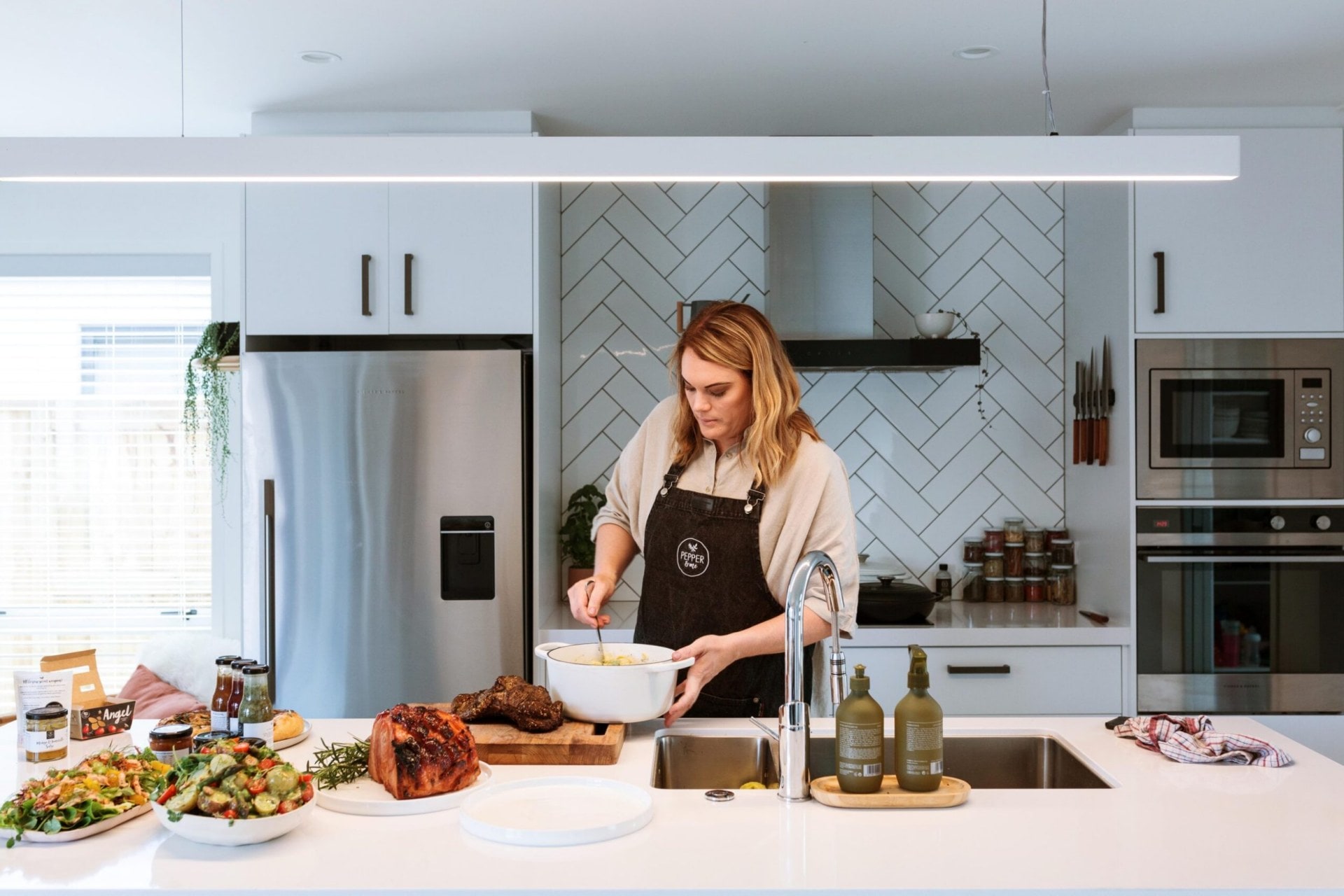 Cherie cooking in her kitchen that has white cabinets, black handles, and white herringbone tiles