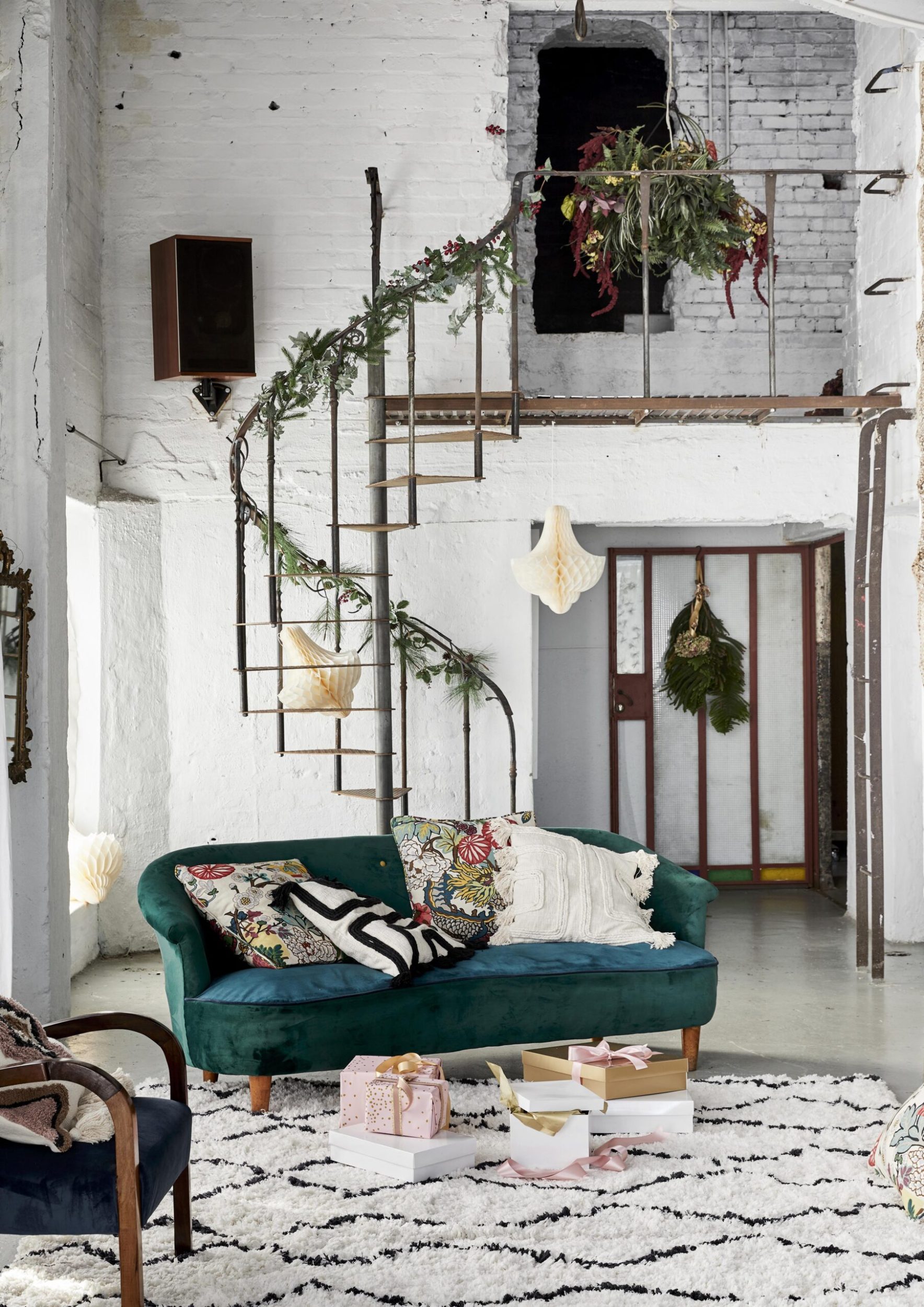 paper decorations hanging from a ceiling and a stairwell, there is a green couch in front of the staircase, a garland hangs around the balustrade