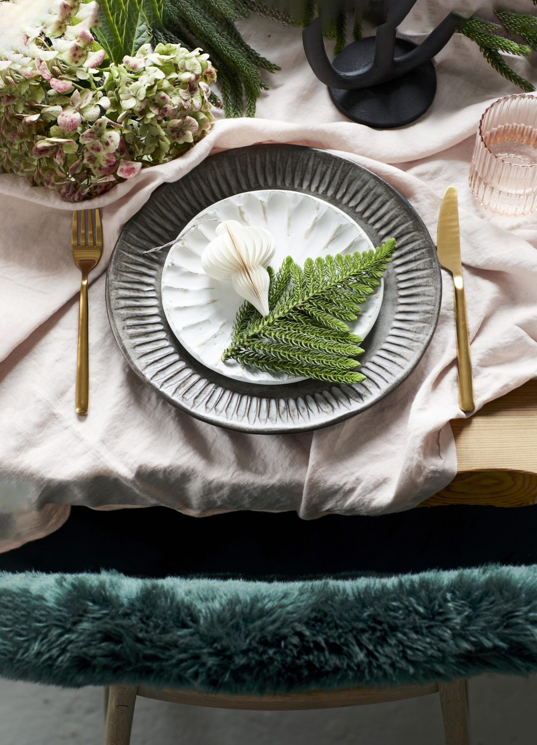 table setting with white plates and a fern as a place holder, a blush tablecloth and gold cutlery