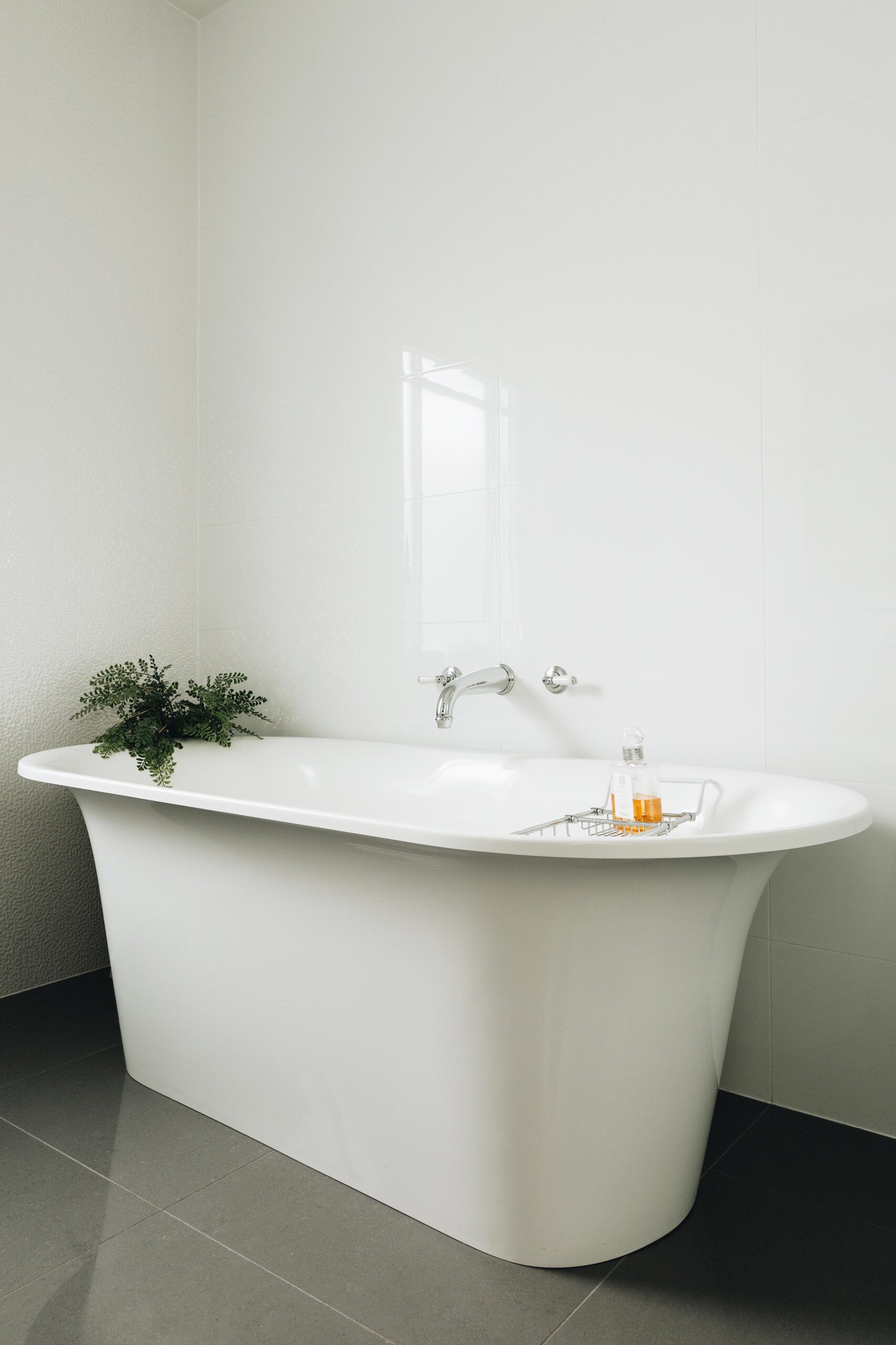 Freestanding bath on grey tiles with glossy white wall tiles