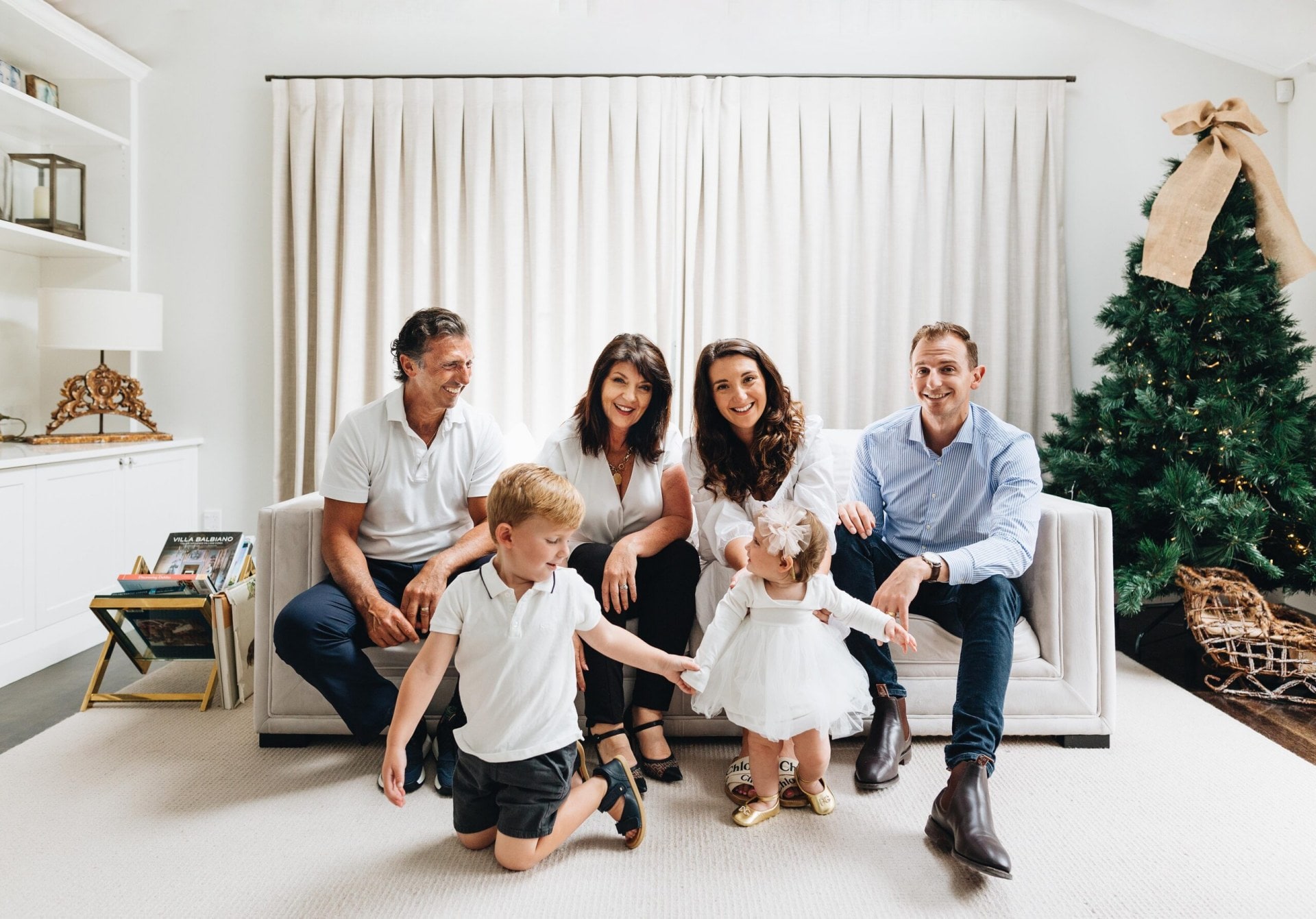 Lisa and Andrew Antonopoulos with their daughter Alexia and her partner Paul sitting on a couch with a white rug on the floor