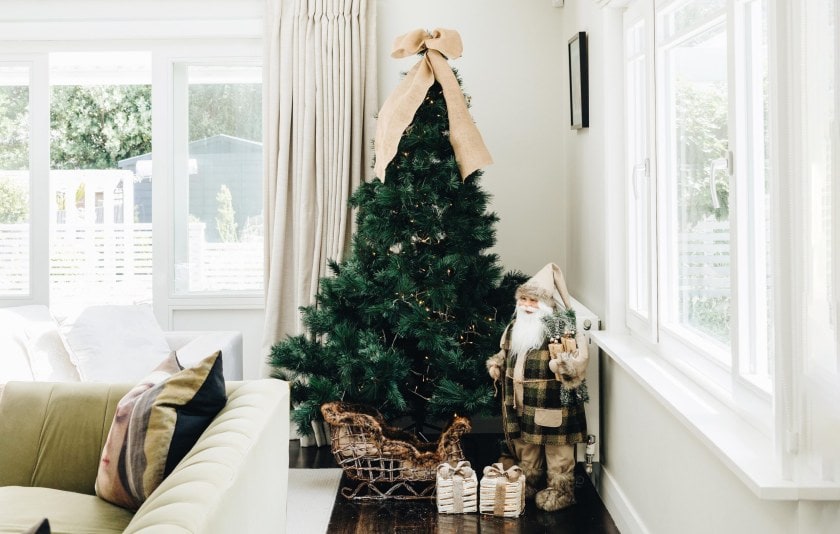 A large Christmas tree with lights and a grey themed Santa sitting next to it