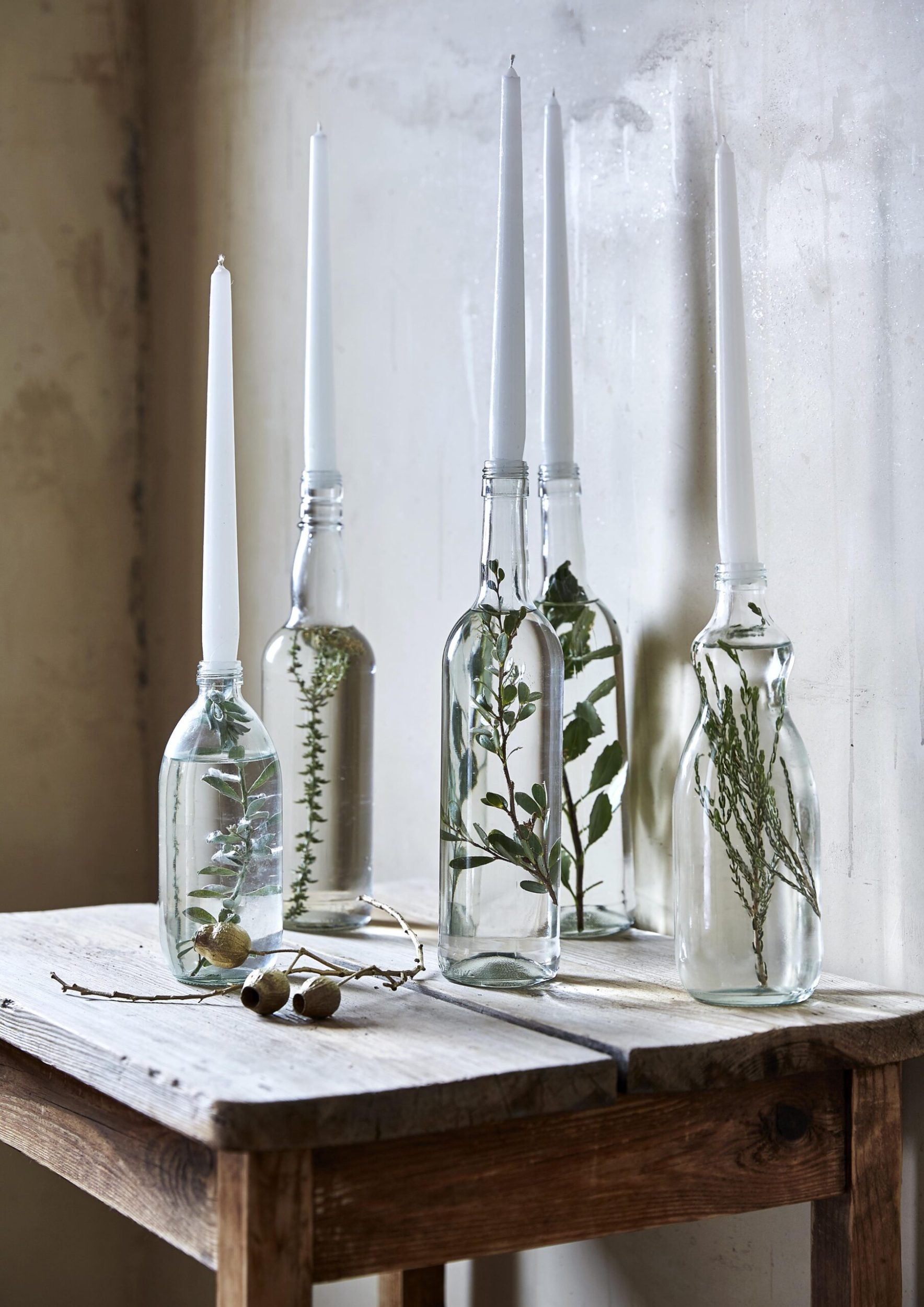 Clear glass bottles filled with water and greenery then with candles from the opening
