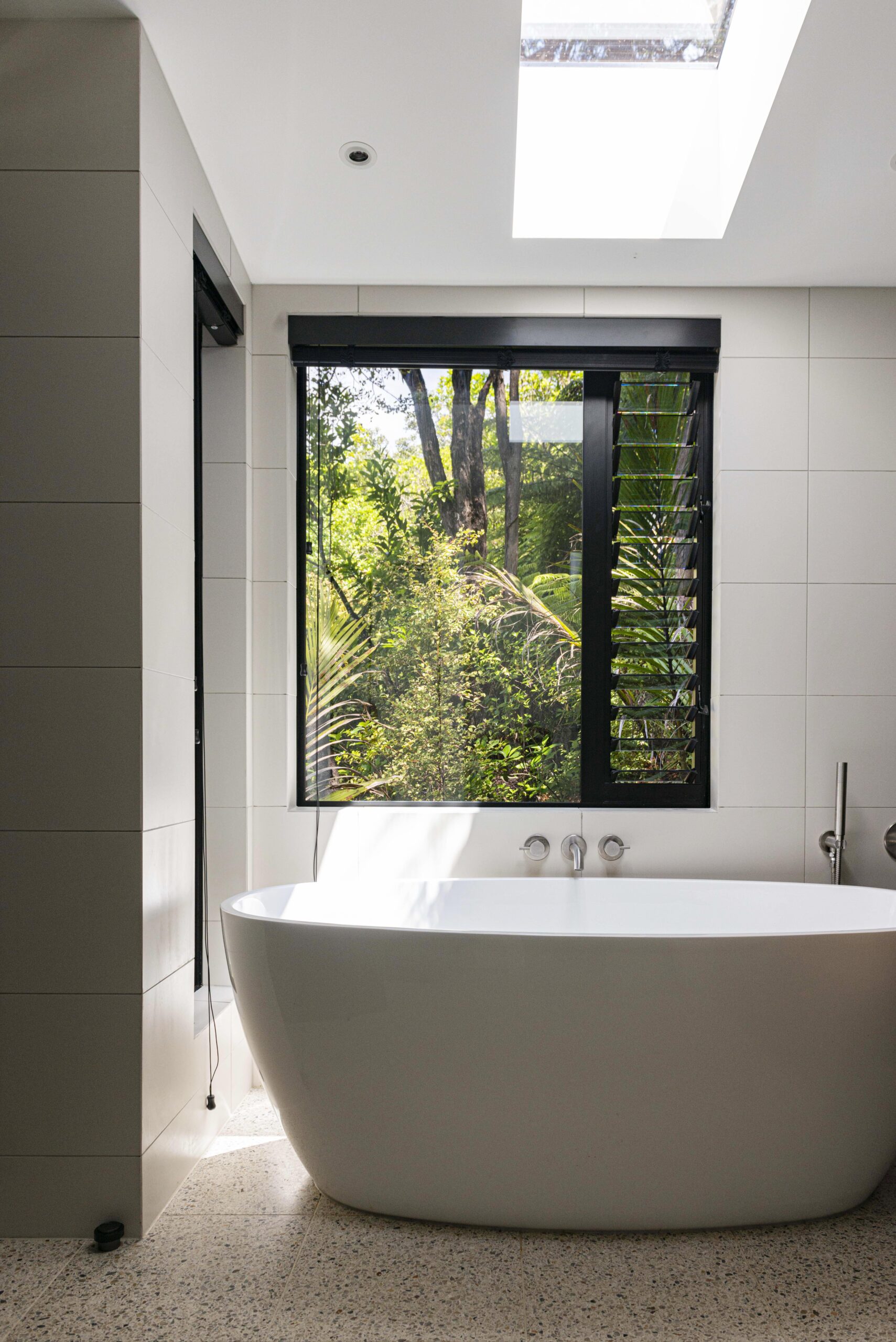 A white bath sitting in front of a large window to allow nature inside