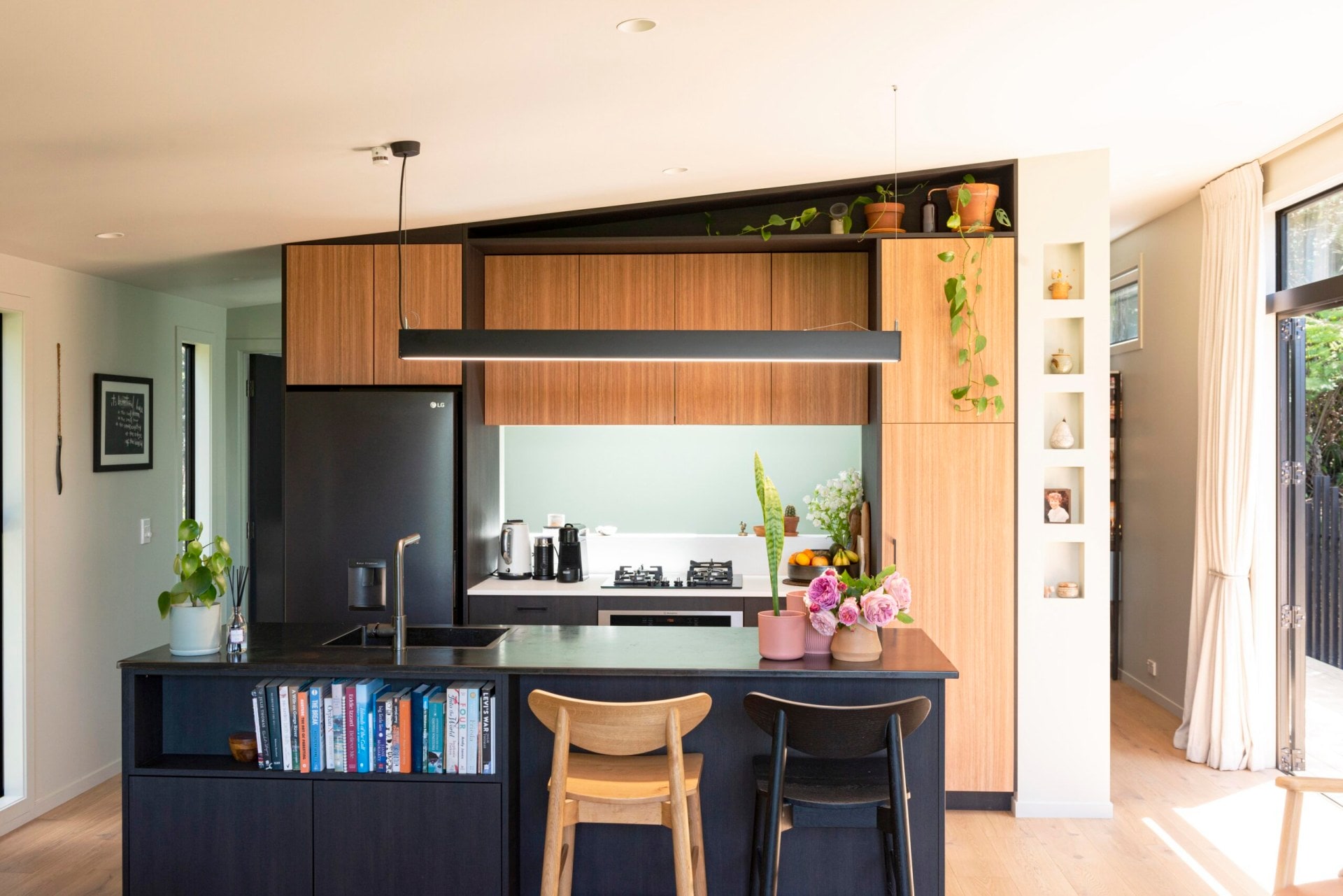 The open plan kitchen with a mix of wood and black cabinets, the ceiling is on a slight slant which comes down into the cabinetry that goes all the way to the ceiling