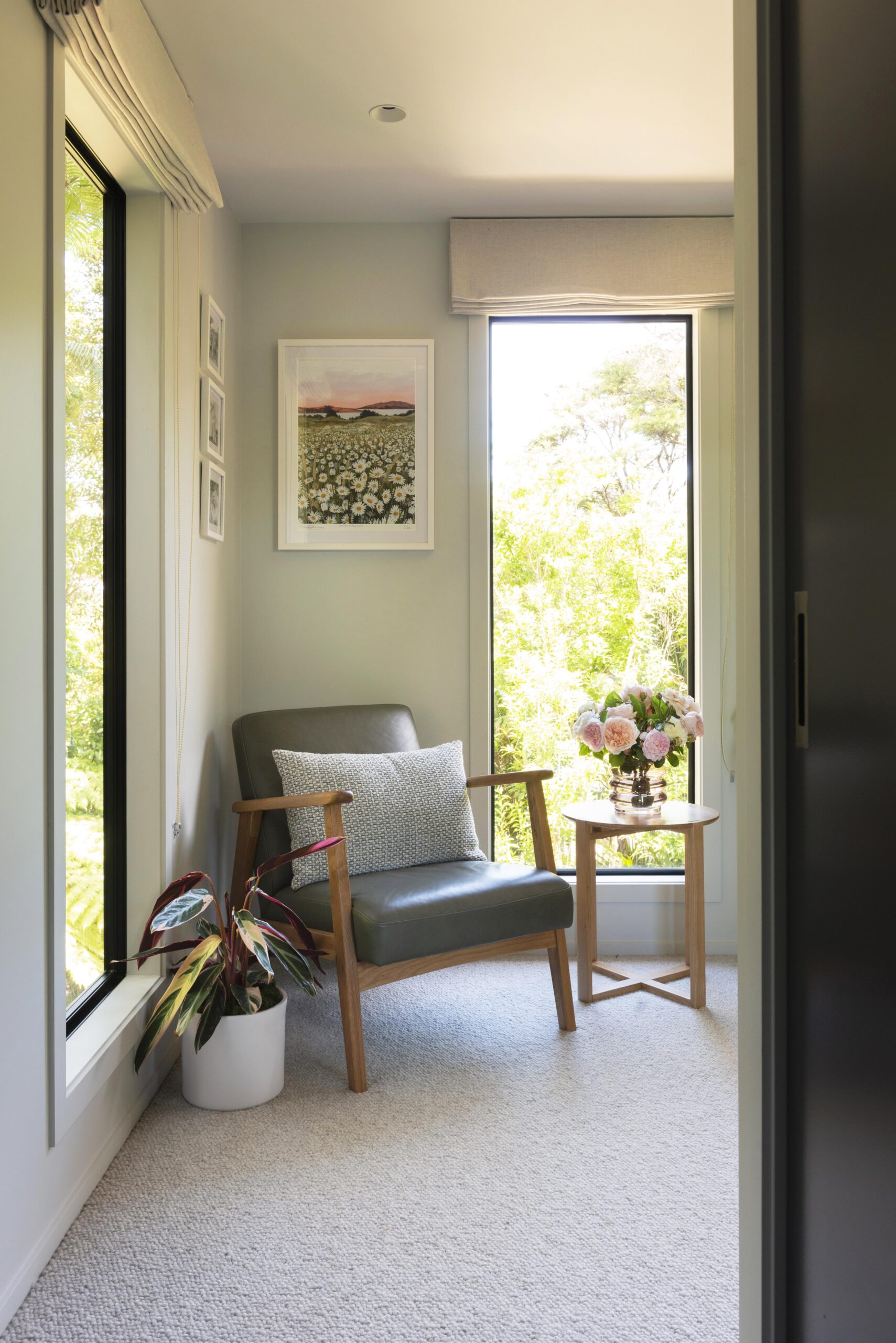 The corner of the bedroom with a leather chair and two windows, art hangs above the chair