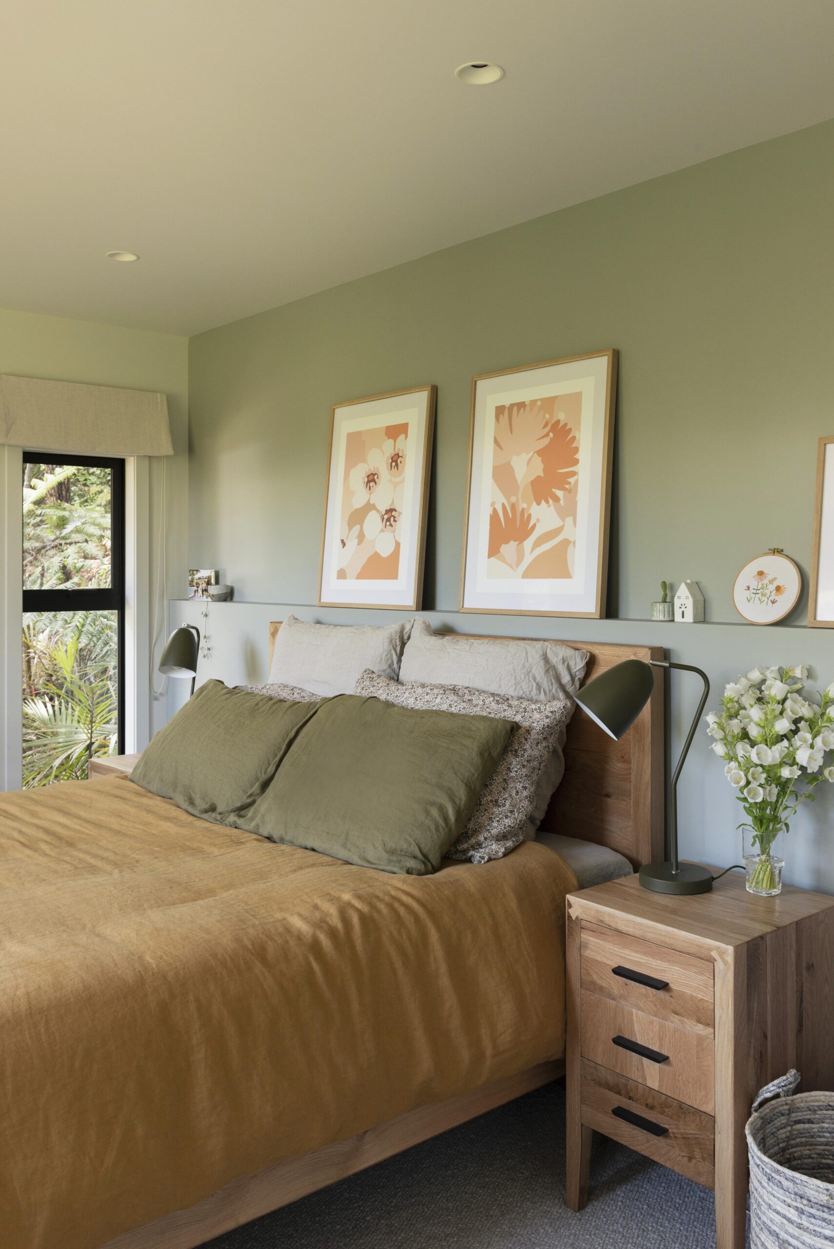 A bedroom with an inbuilt shelf headboard, artwork along it, green walls, rust bed linen